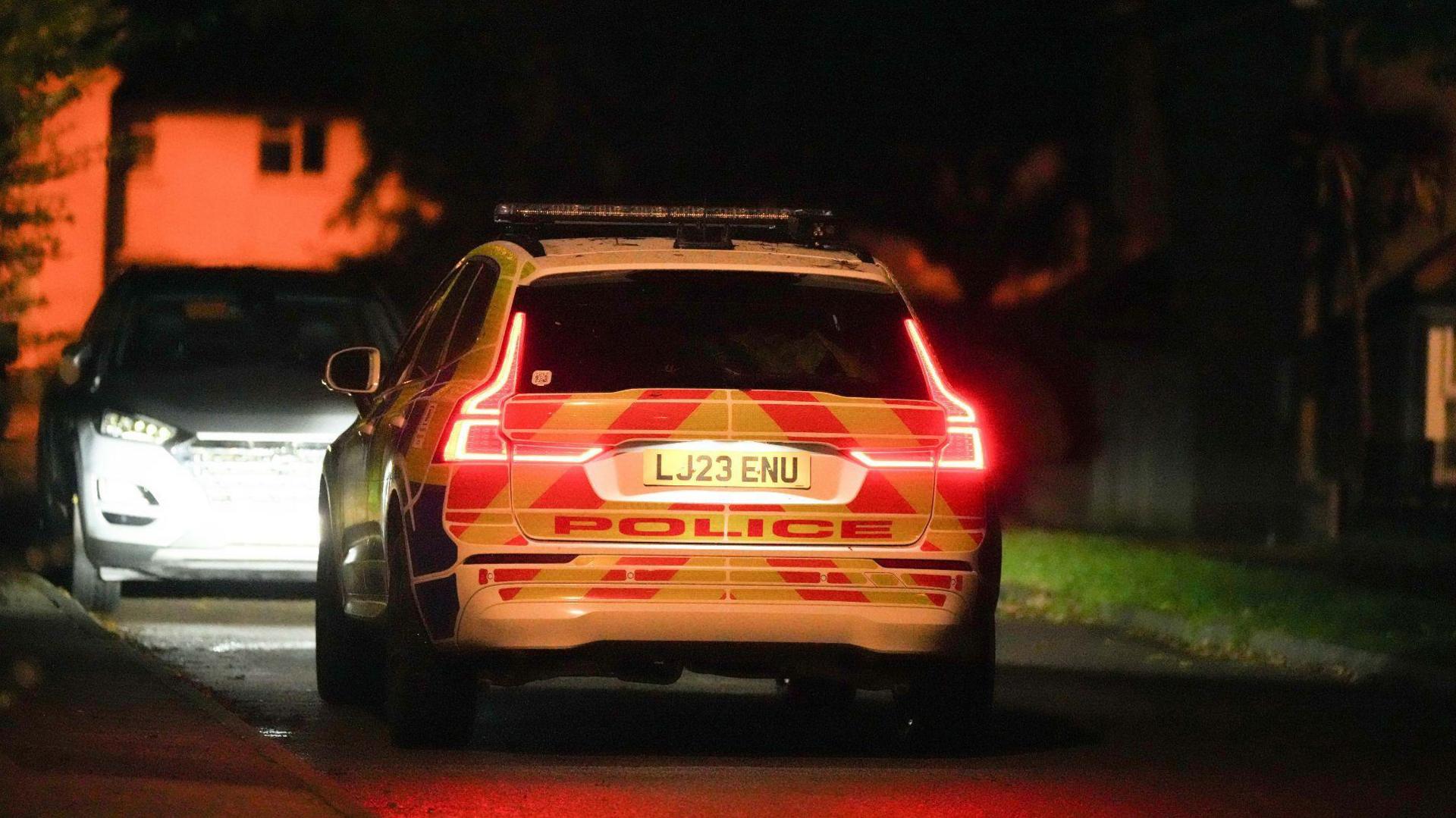 The back of a large police vehicle, with the word police written on it. There are yellow and red diagonal stripes on the back. The rest of the image is not visible as it is dark