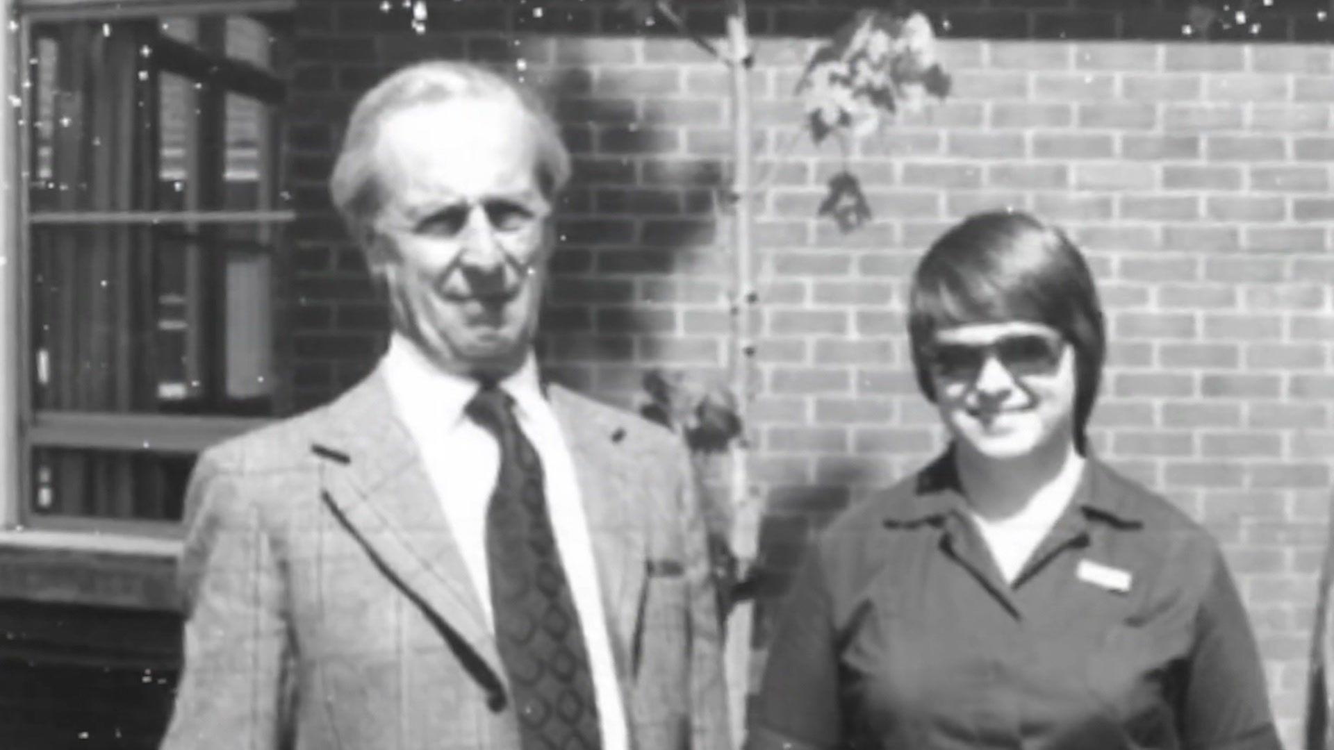 A black and white image of Doctor Ronald Fisher and a younger female nurse. Dr Fisher is dressed in a 1970s style suit.