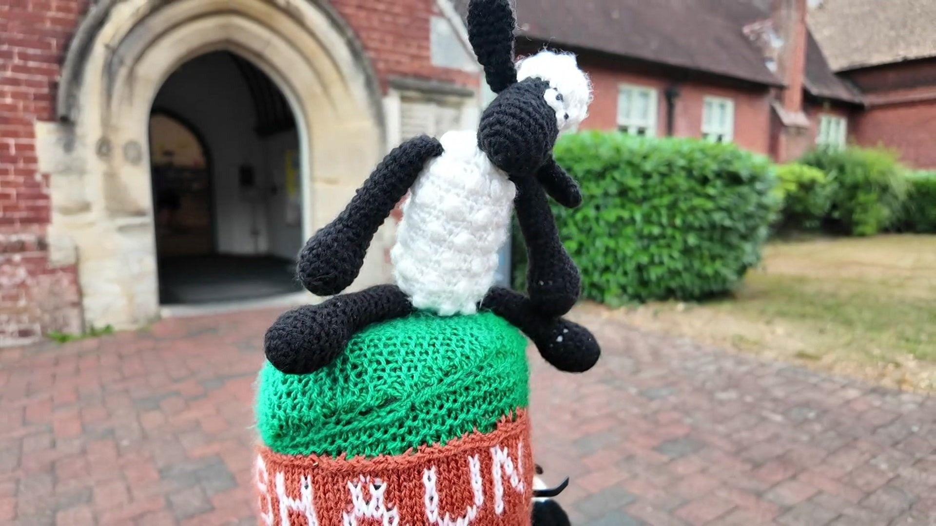 A woollen Shaun the Sheep character on a bollard in front of a church
