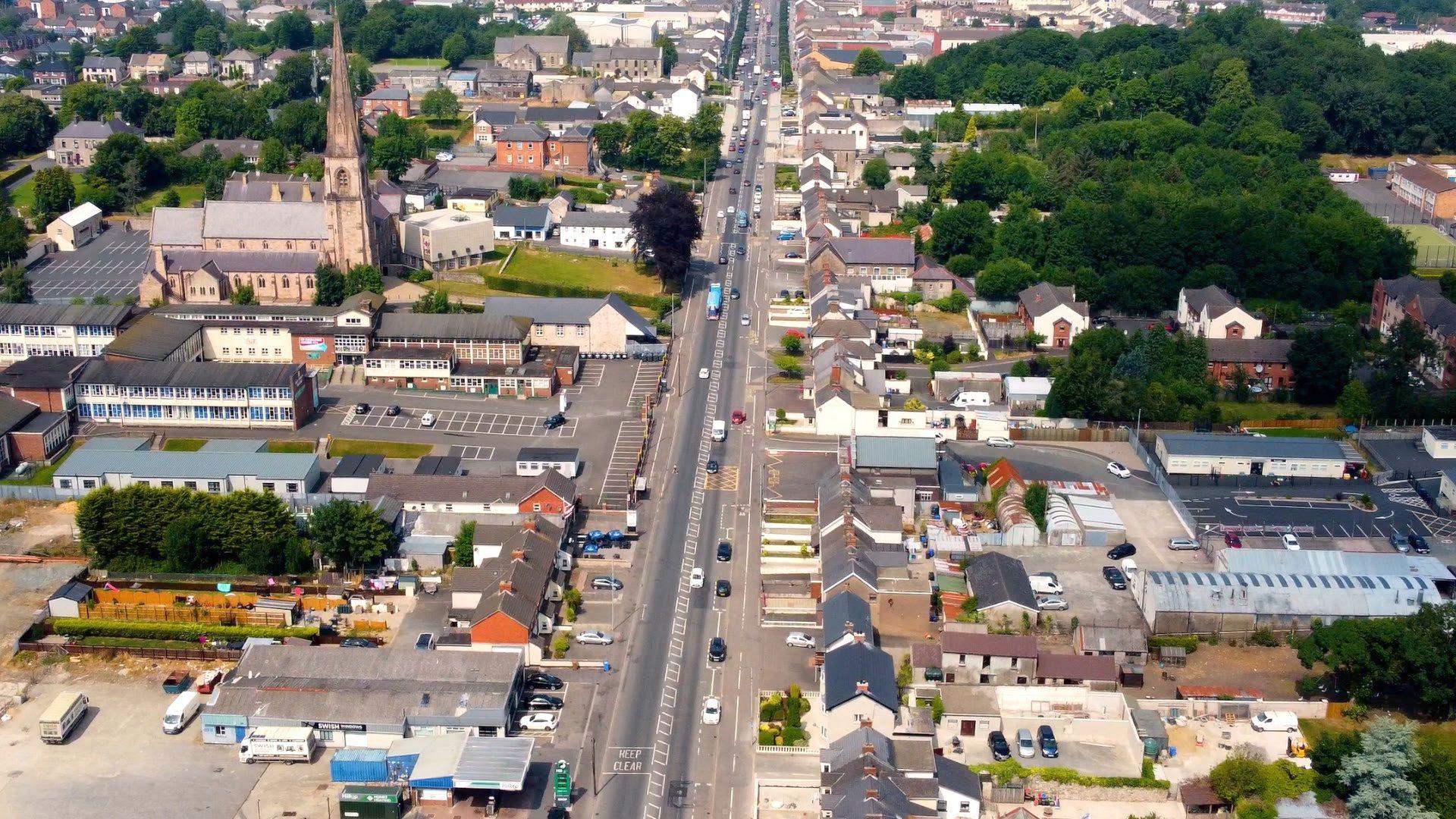 A drone image of the main street in Cookstown. Cars travel down the road and there are buildings, trees and a church on either side. 