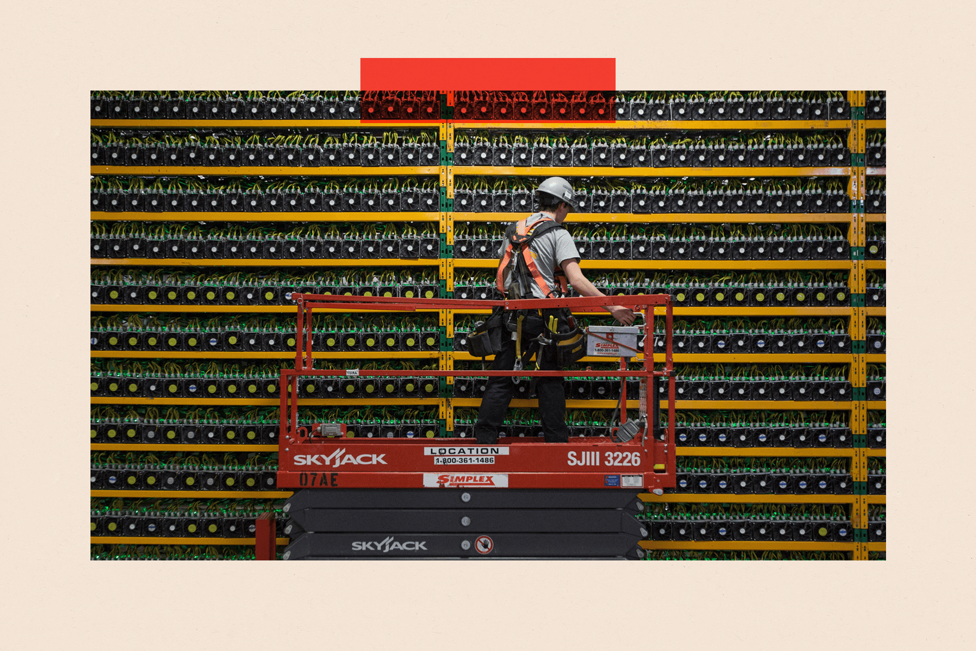 A man in a safety helmet stands on a platform in front of a bank of Bitcoin mining computers