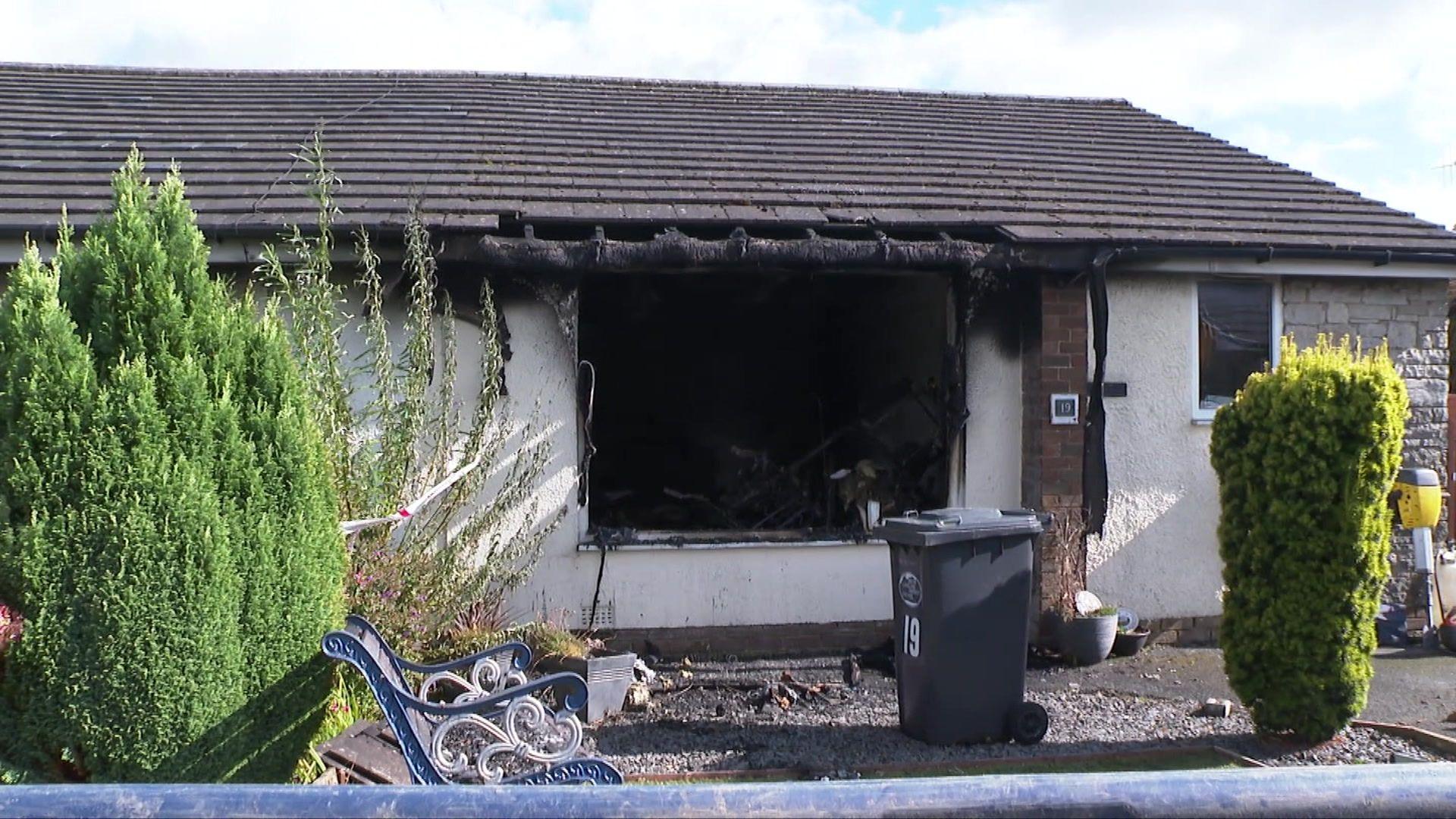 A white stone bungalow has a black, sooty hole where a window used to be. Soot marks can also be seen to have reached the roof.