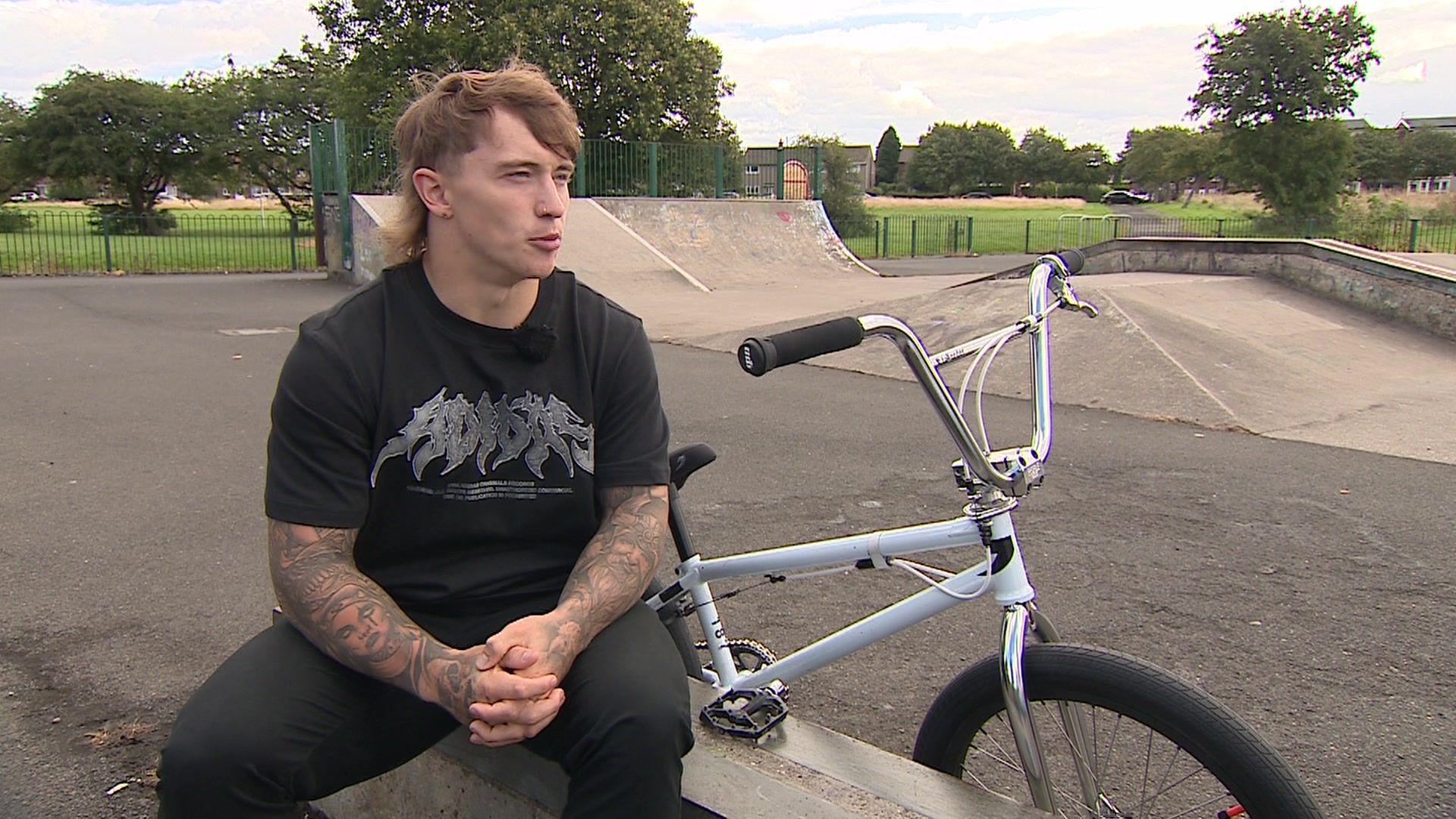 Kieran Reilly sat next to his BMX in Leam Lane skate park in Gateshead. A concrete quarter pipe and box jump can be seen behind him