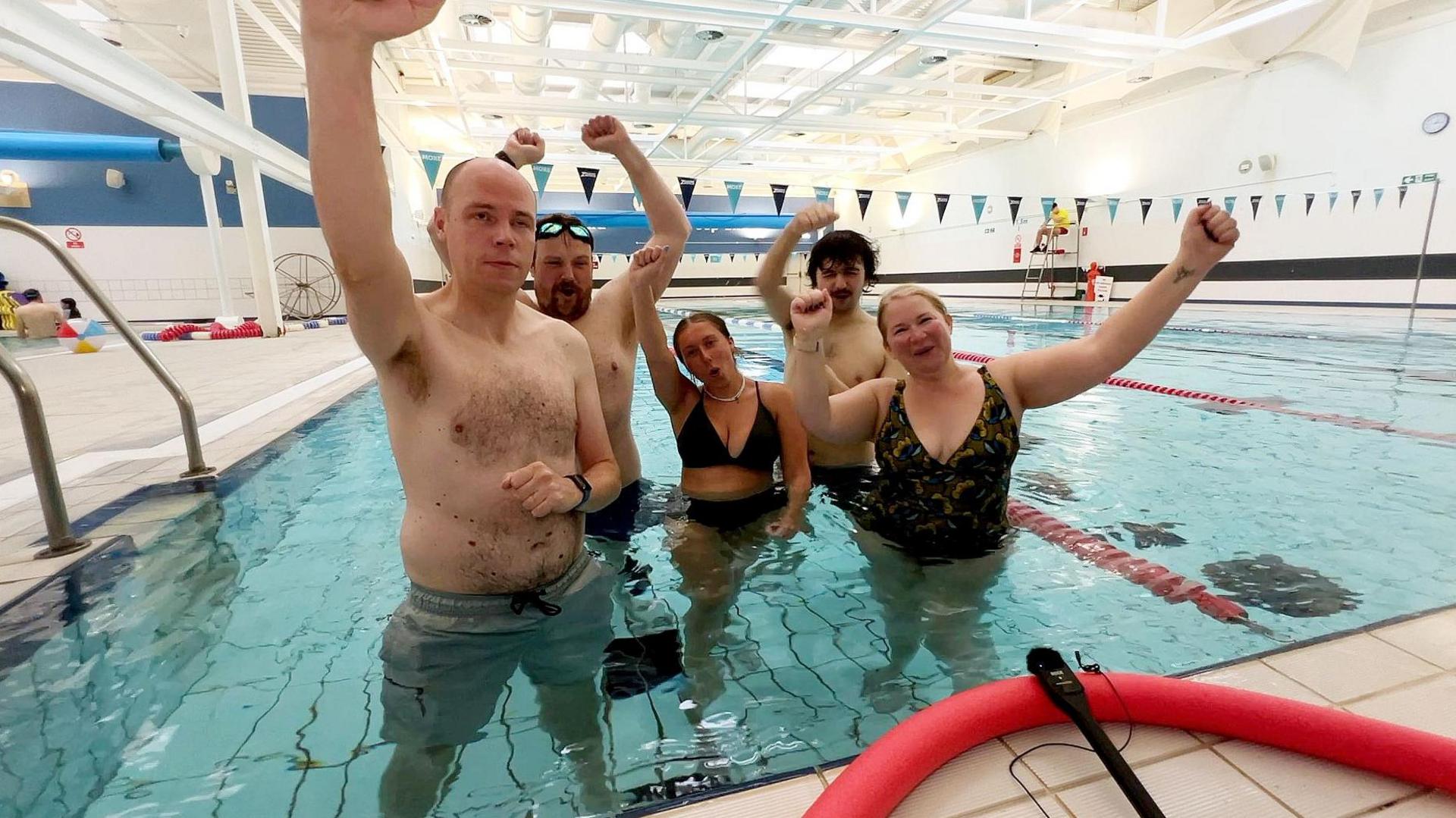 The team celebrate completing the swim challenge in the pool, looking happy, relieved, and triumphant.