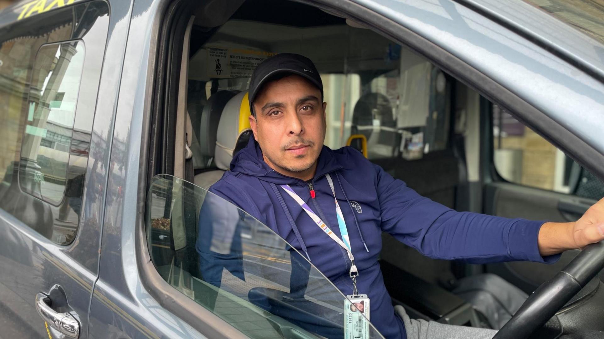 A taxi driver behind the wheel of his cab looks out the window