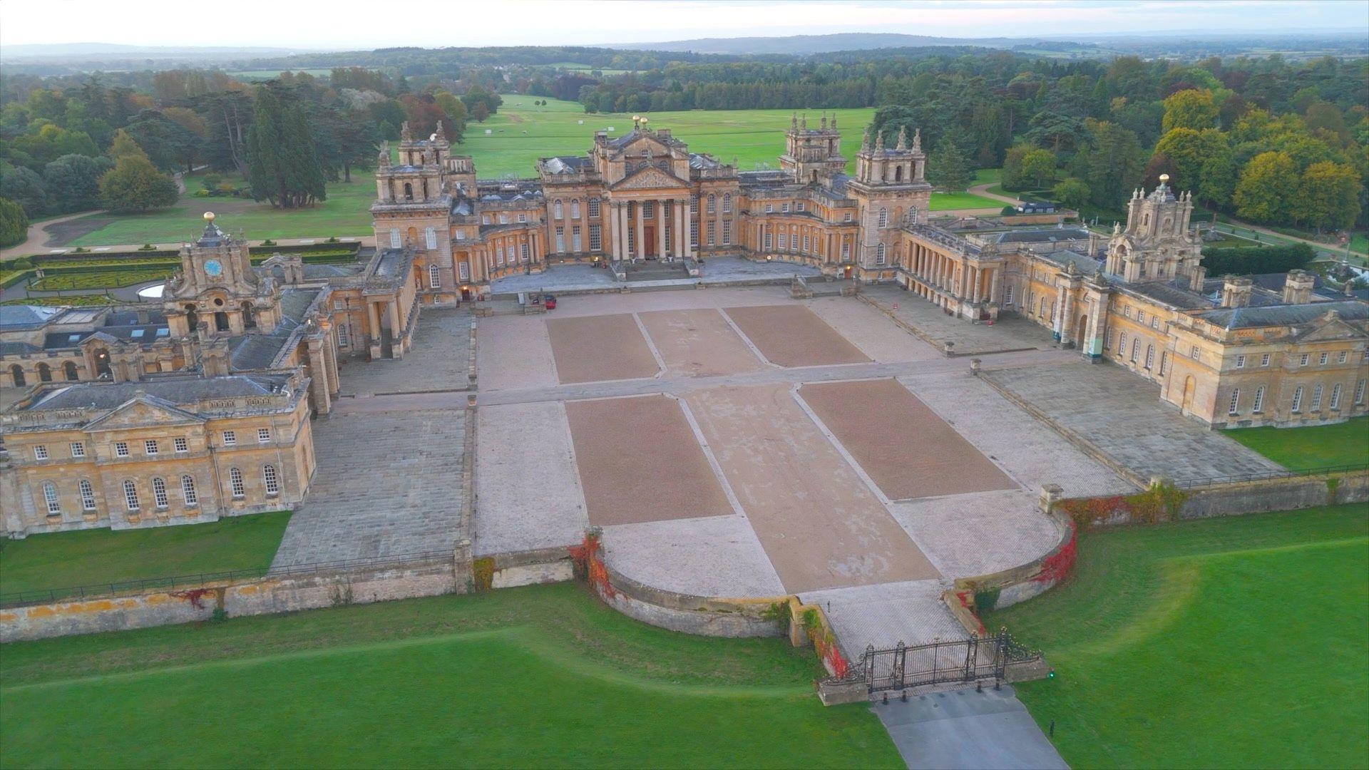 A picture of a very large baroque palace seen from the sky. There are green fields all around the palace. 