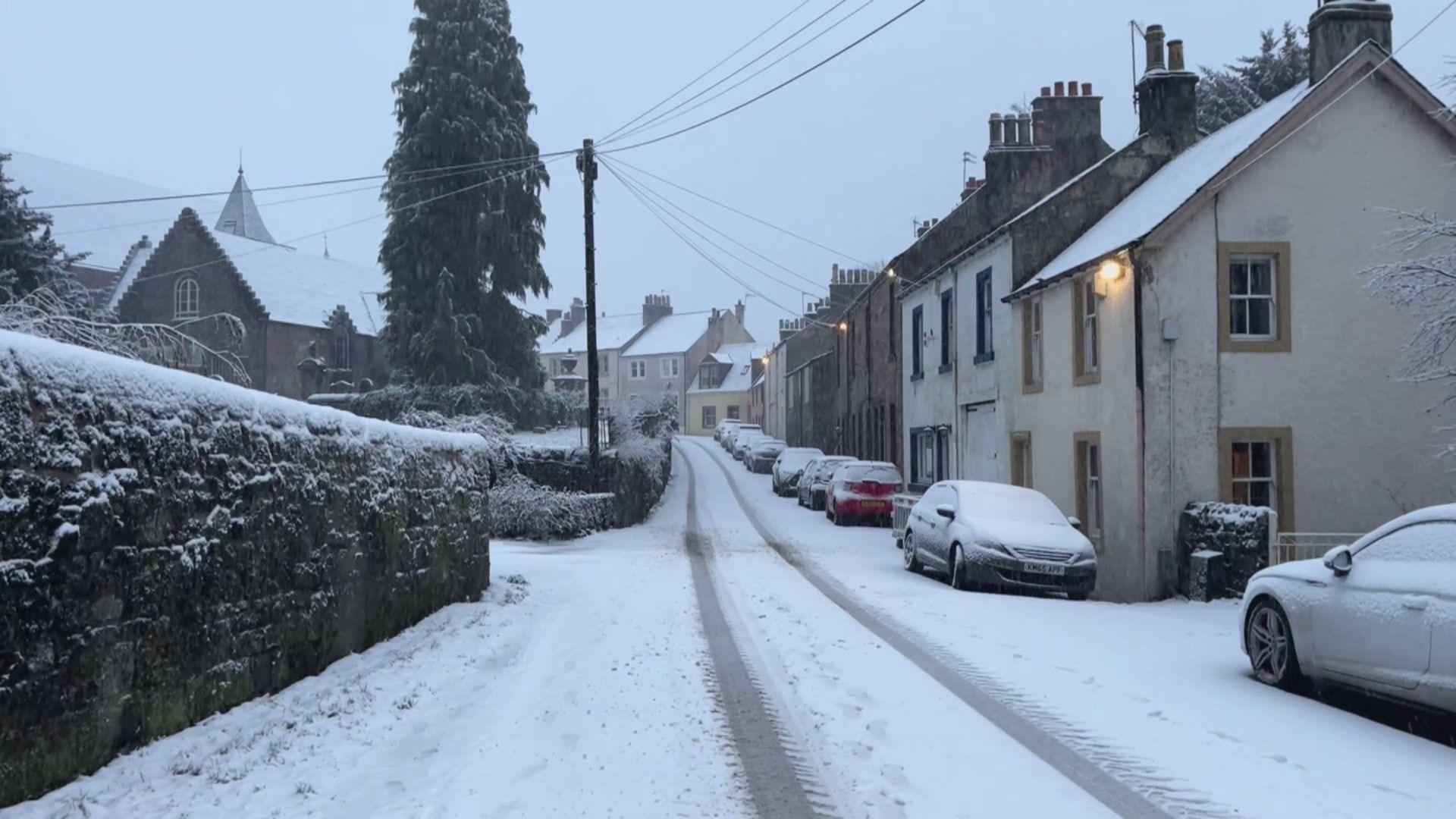 Village in Scotland, with cars, walls and roads covered in snow.