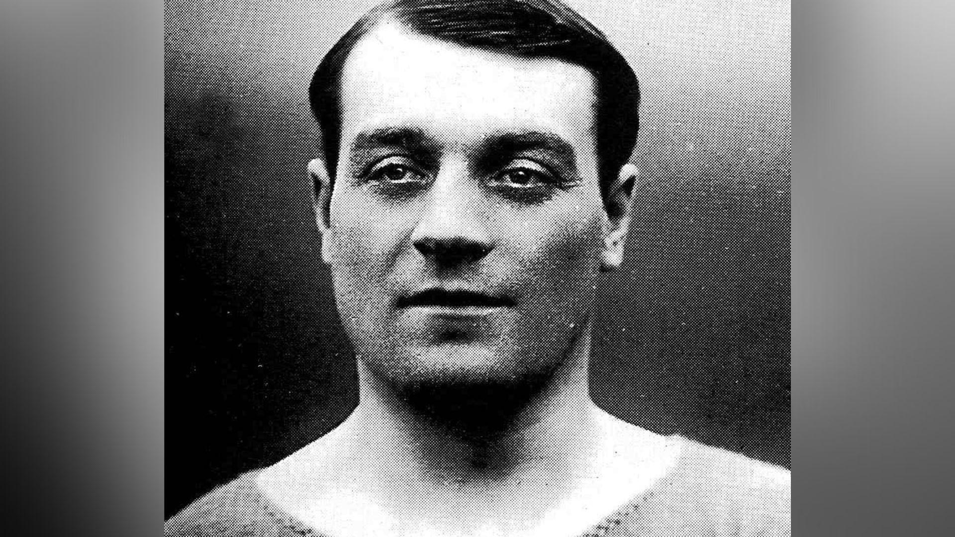 A black and white photo of a dark-haired man in a shirt.