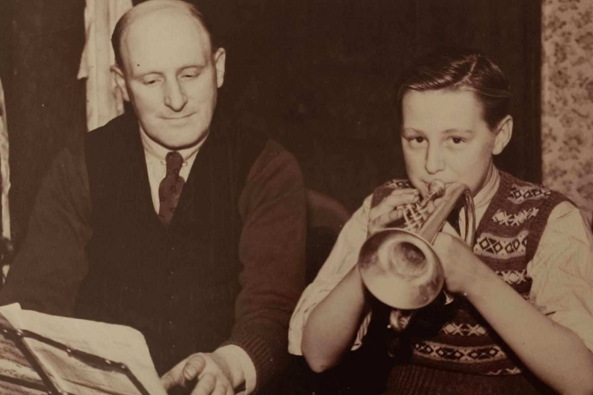 Ms Grayson's father Graham pictured playing a trumpet while his father Harold turns a music sheet