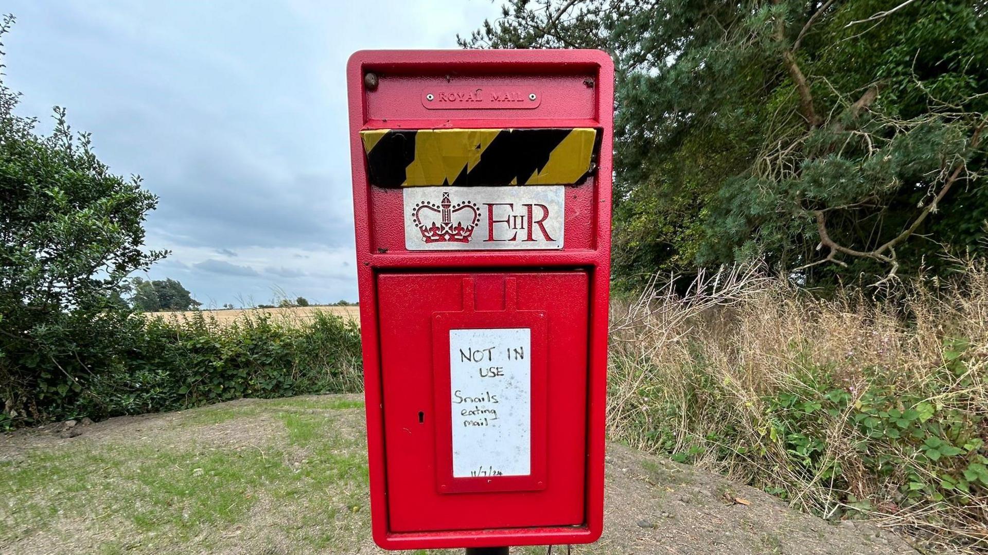 A post box with a sign on it saying 'NOT IN USE - snails eating mail' - with the date of 11 July 2024 on it 