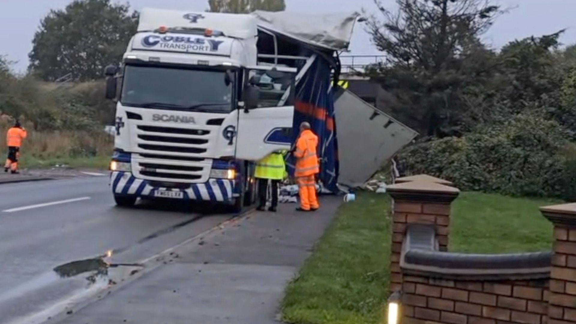 White HGV stationary on a single carriageway road with the trailer open and quantities of cargo spilling on to road