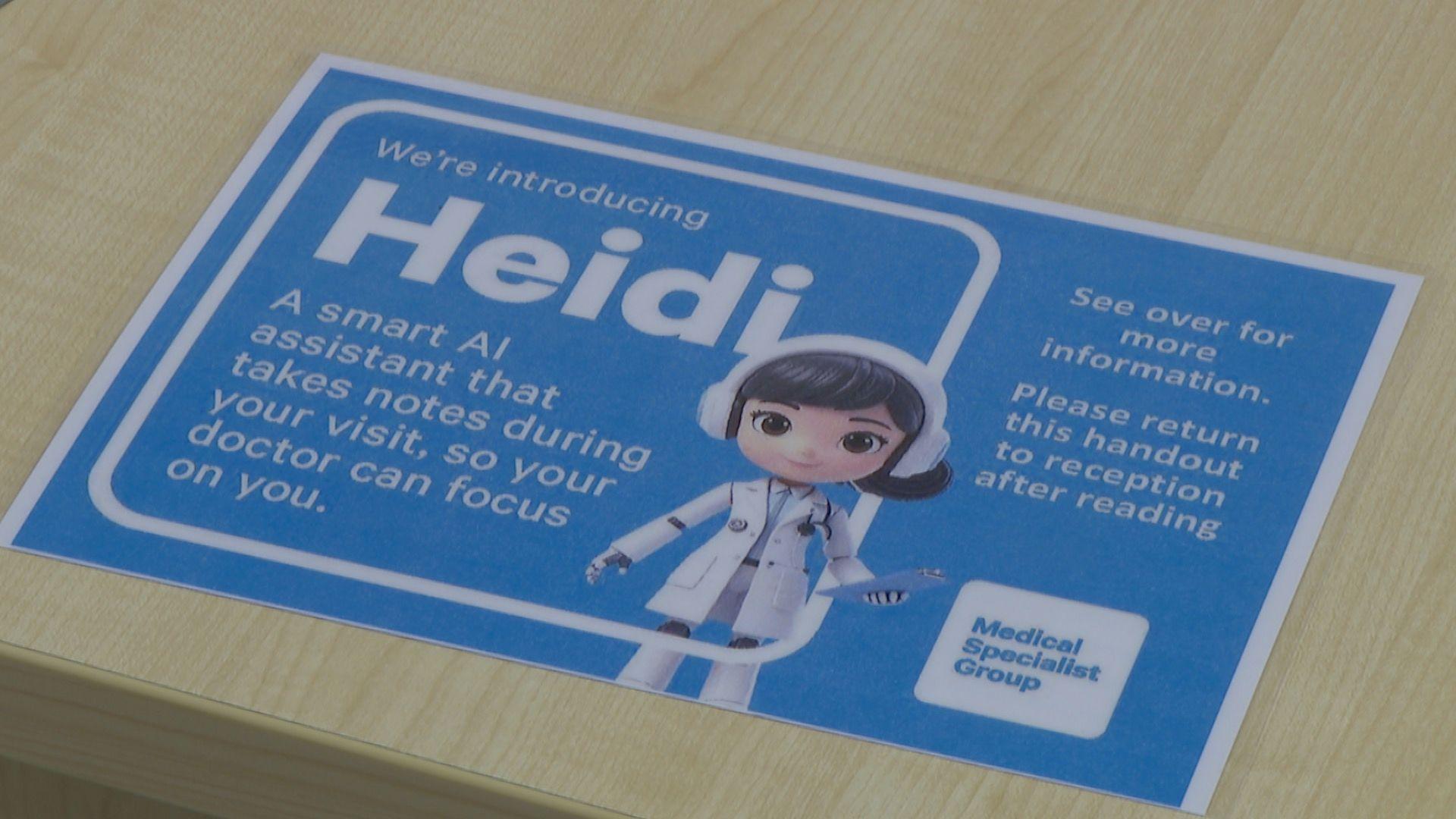 A blue piece of paper sits on a wooden desk. It explains that Guernsey's MSG are using a smart AI assistant, known as Heidi.