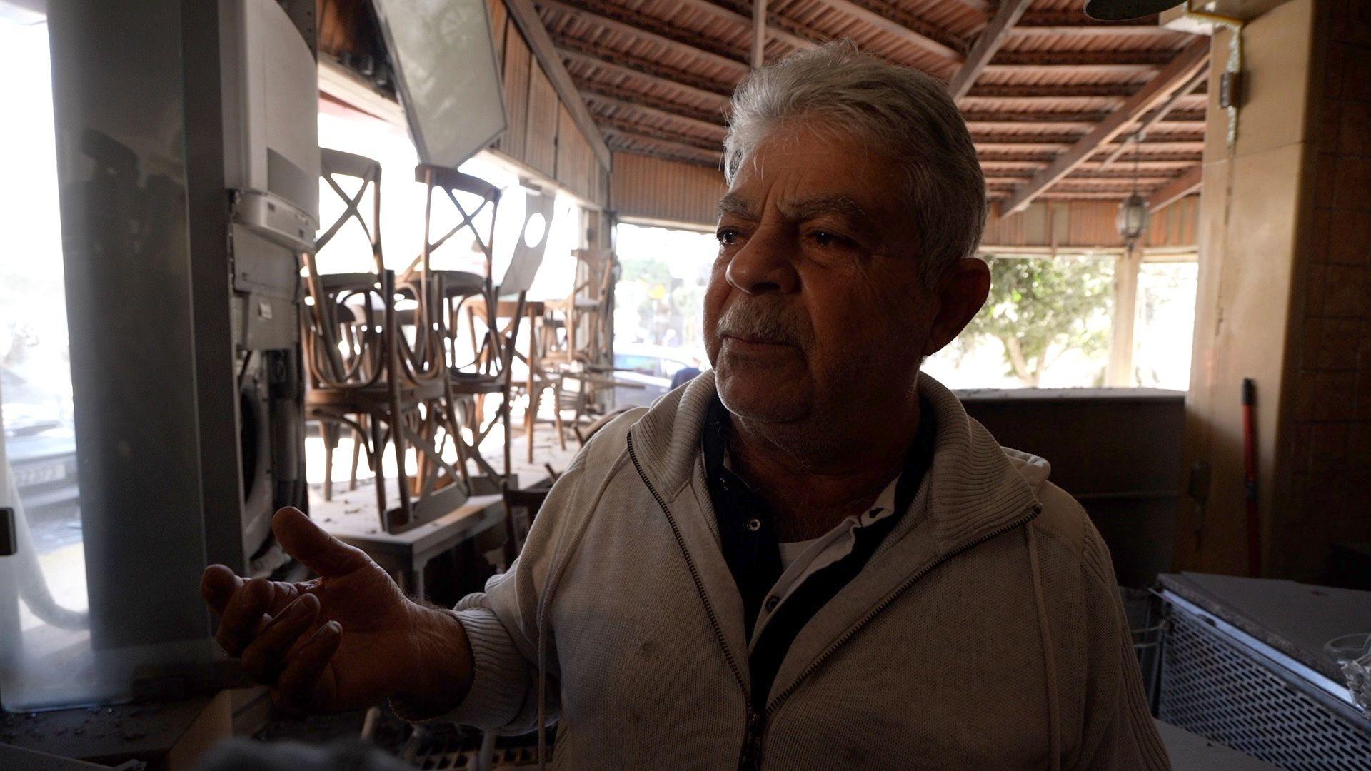 Restaurant-owner Deed Badawi inside his restaurant that has been damaged. He is talking, gesturing with his right hand.