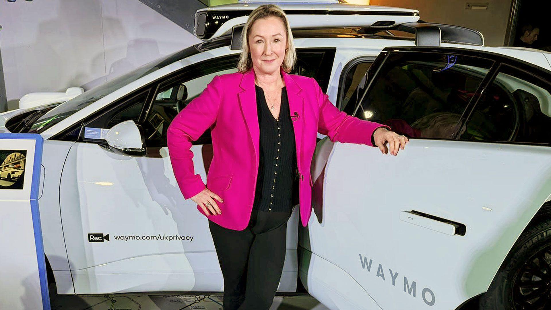 BBC technology editor Zoe Kleinman stands in front of a white car, wearing a red jacket over a black top and black trousers 