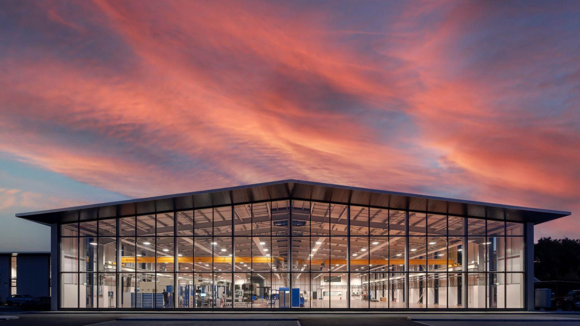 A pink sunset over a large warehouse-type building, with a huge glass front.