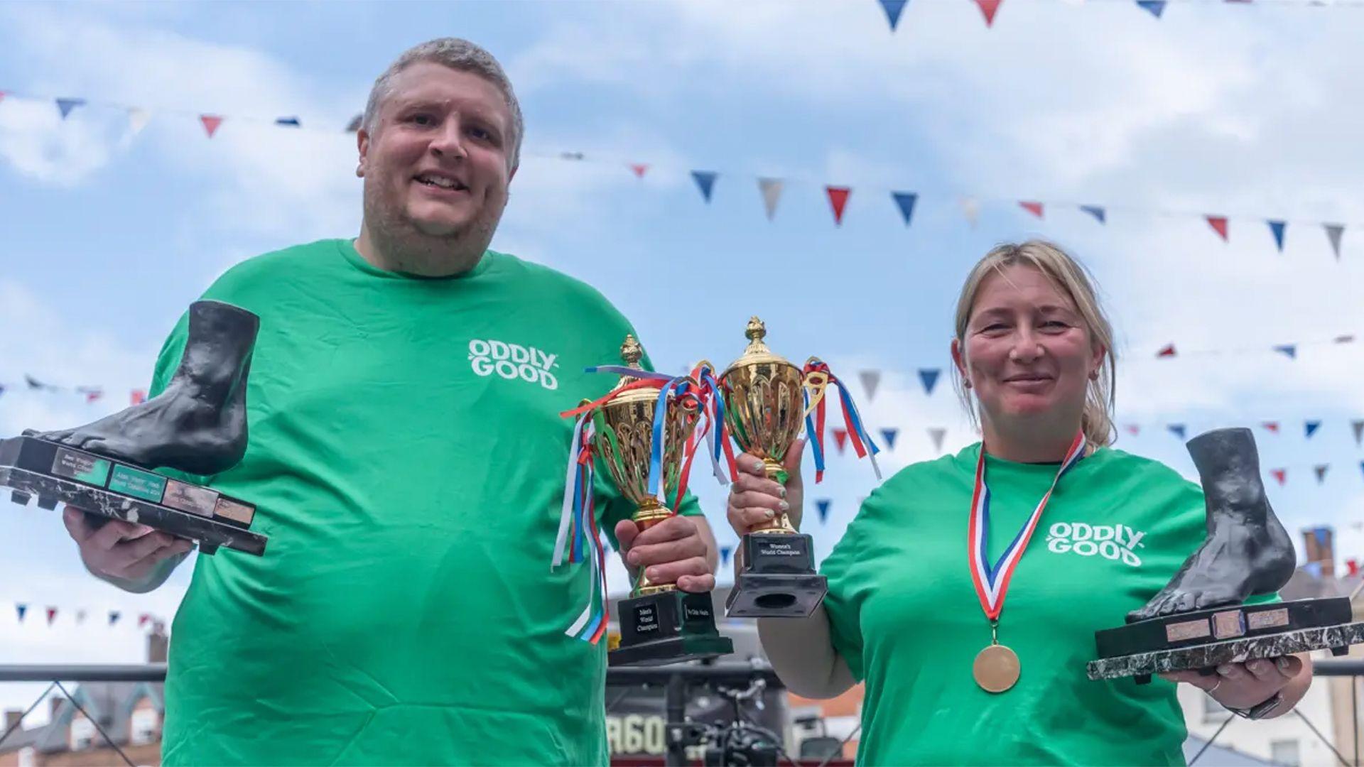 Toe Wrestling Championship reigning champions Ben Woodroffe and Lisa Shenton hold up foot-shaped trophies outside in Fenny Bentley.