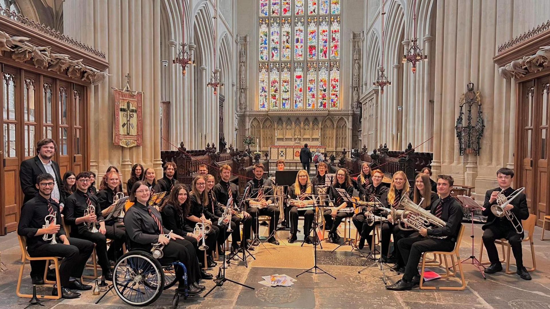 Ianto Williams (far left) with the rest of the universities brass band. They are performing in a church hall and are all looking at their camera holding their instruments. 