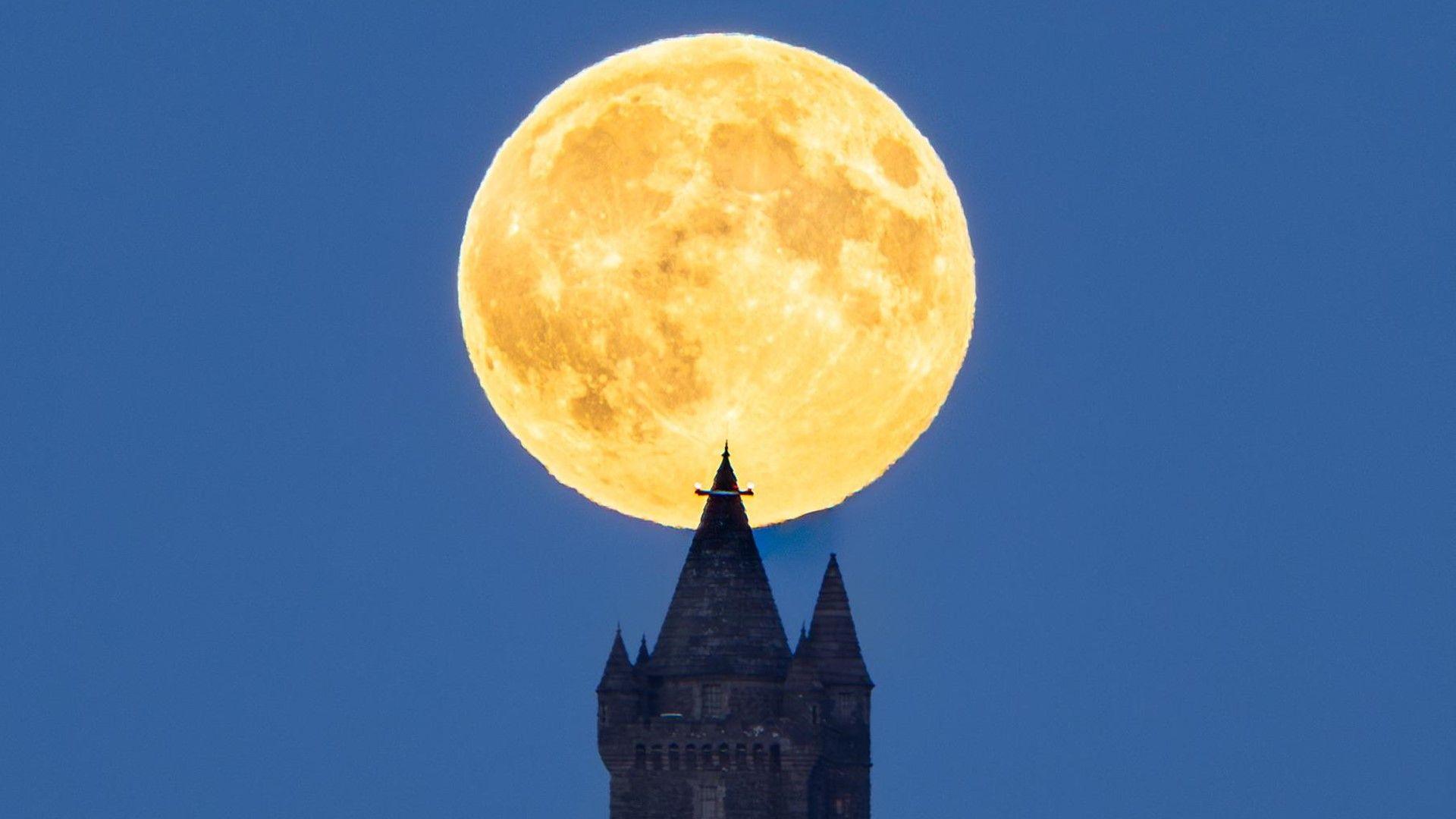 Orange hue to the full moon rising behind a church tower