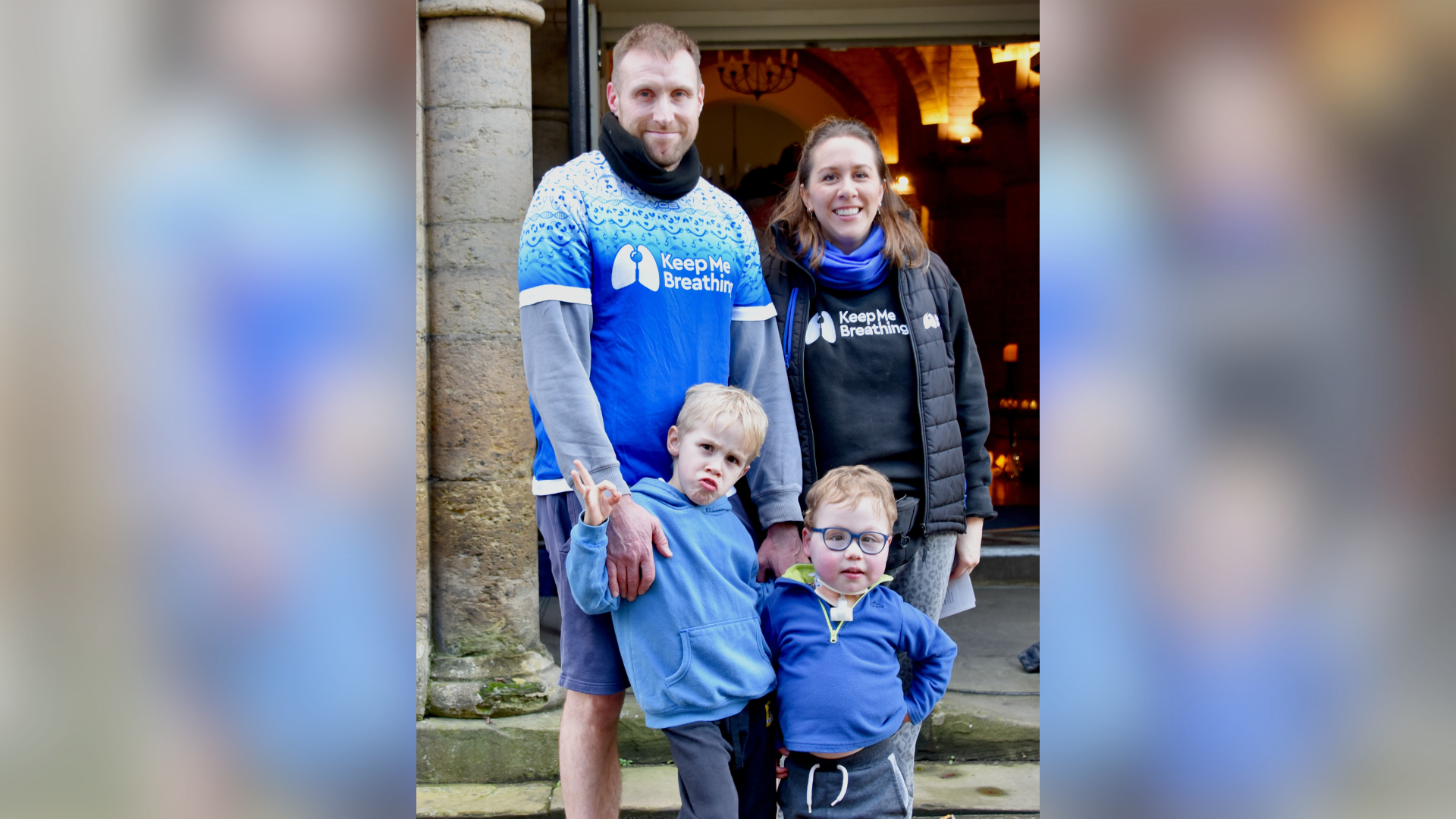 A family stood together wearing blue and black shirts reading "Keep Me Breathing".