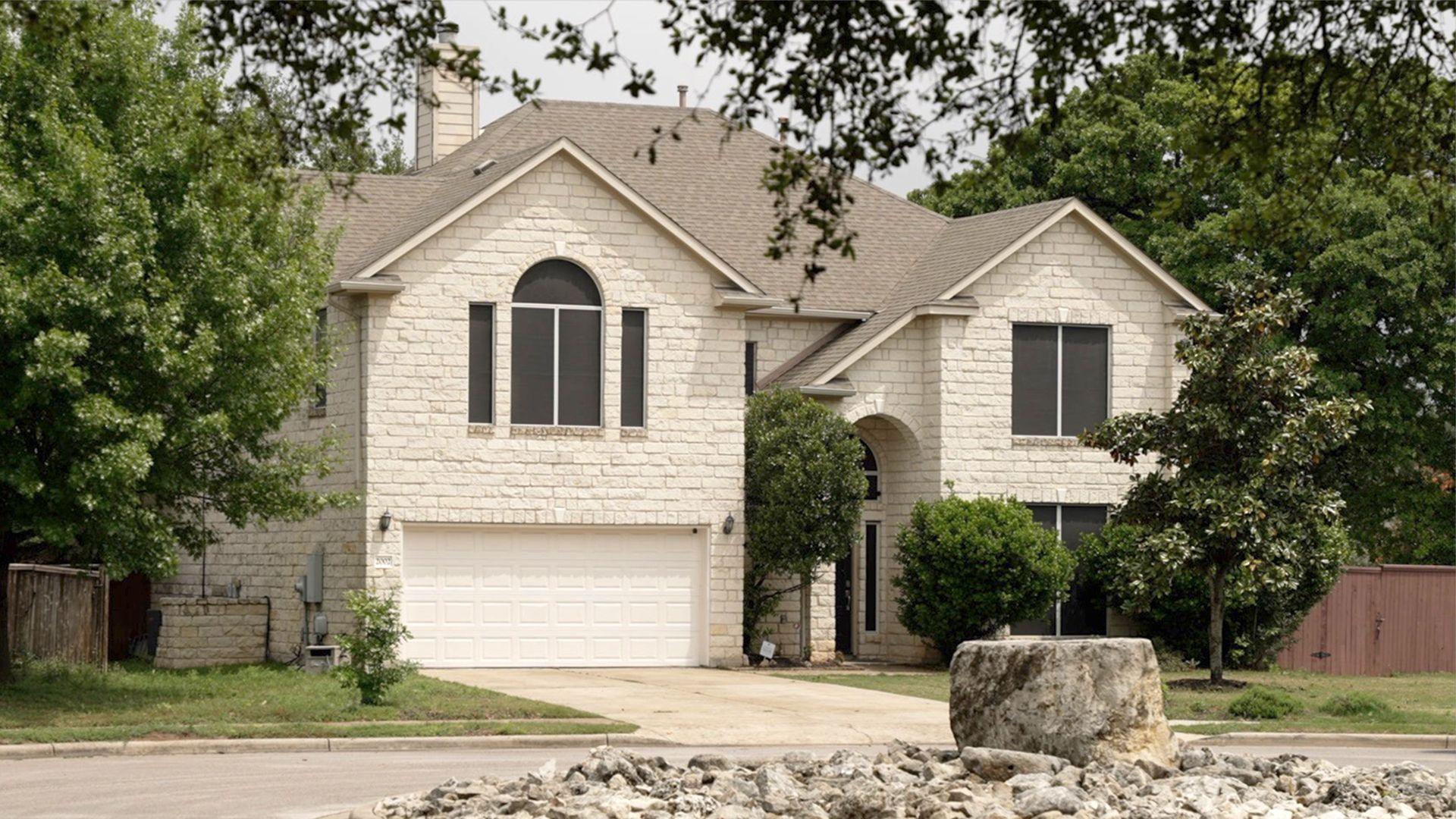 Large beige suburban house in Austin, Texas, surrounded by trees