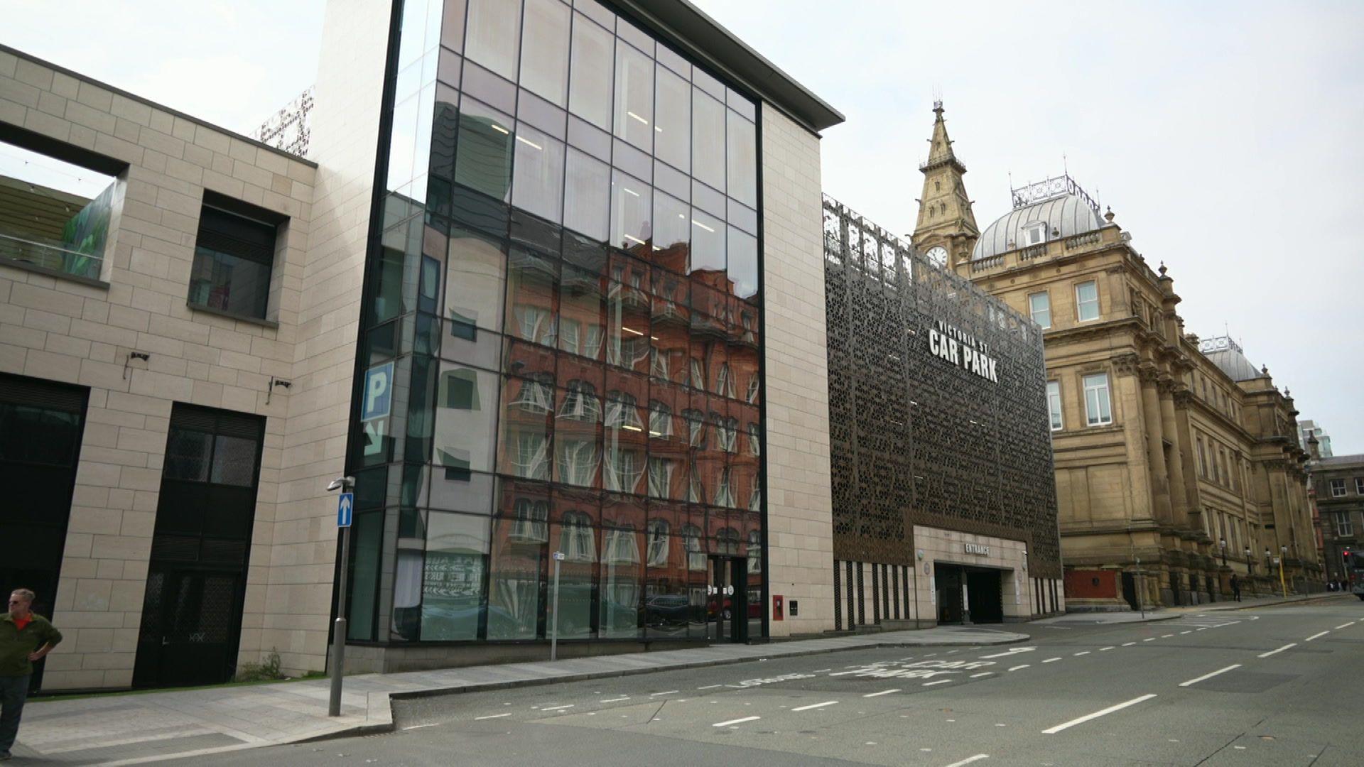 Image shows the Victoria Street car park in Liverpool. It is a relatively recently built building with a glass wall and then a steel mesh covering the sides of the car park itself. The former Municipal Building of Liverpool city council is behind the car park, further up the hill.