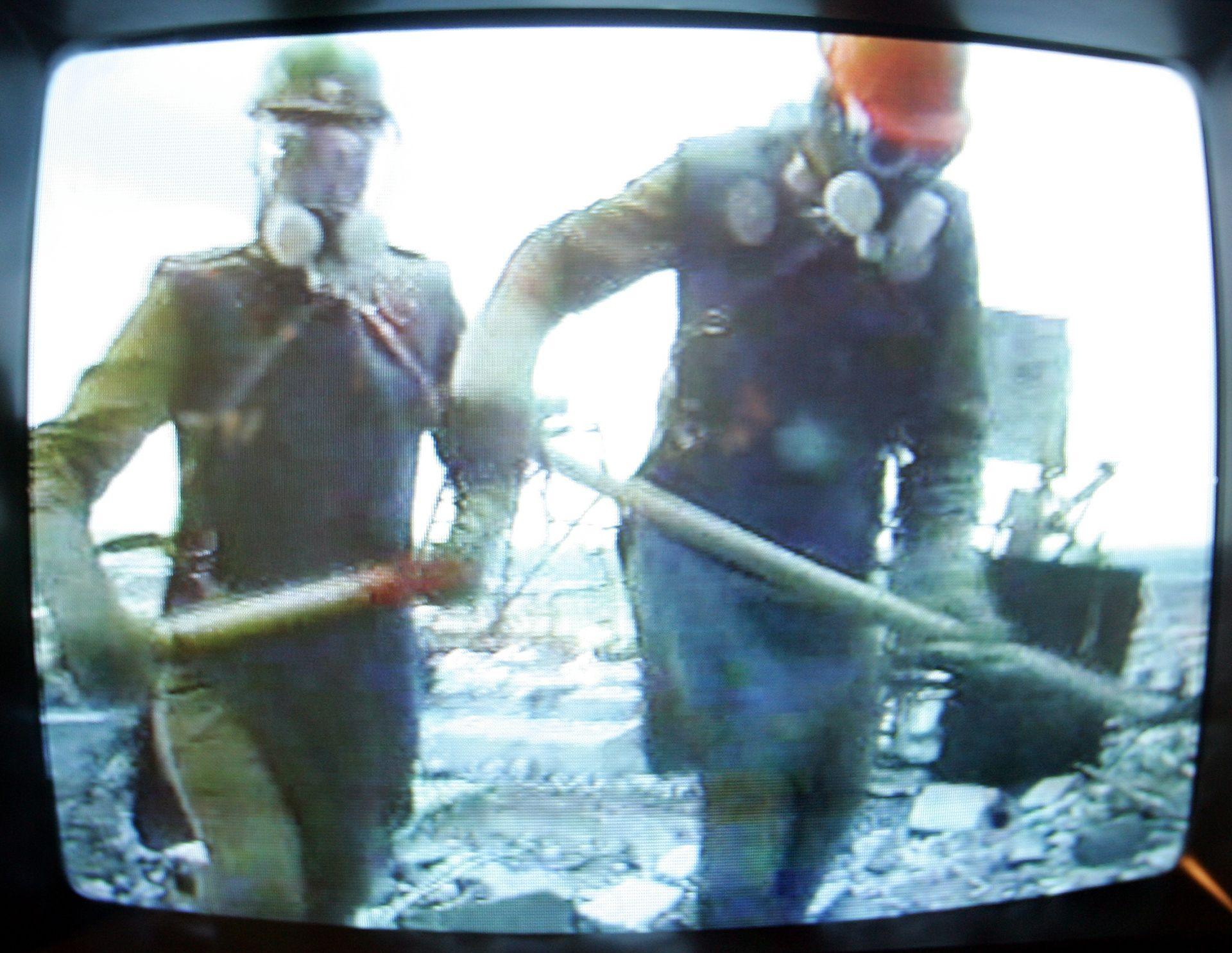 A TV at the Chernobyl museum in Kiev shows a documentary film about the liquidators. Framed by the black edges of an old-style television set, the image shows two men in lead aprons, construction helmets and respirators carrying shovels.
