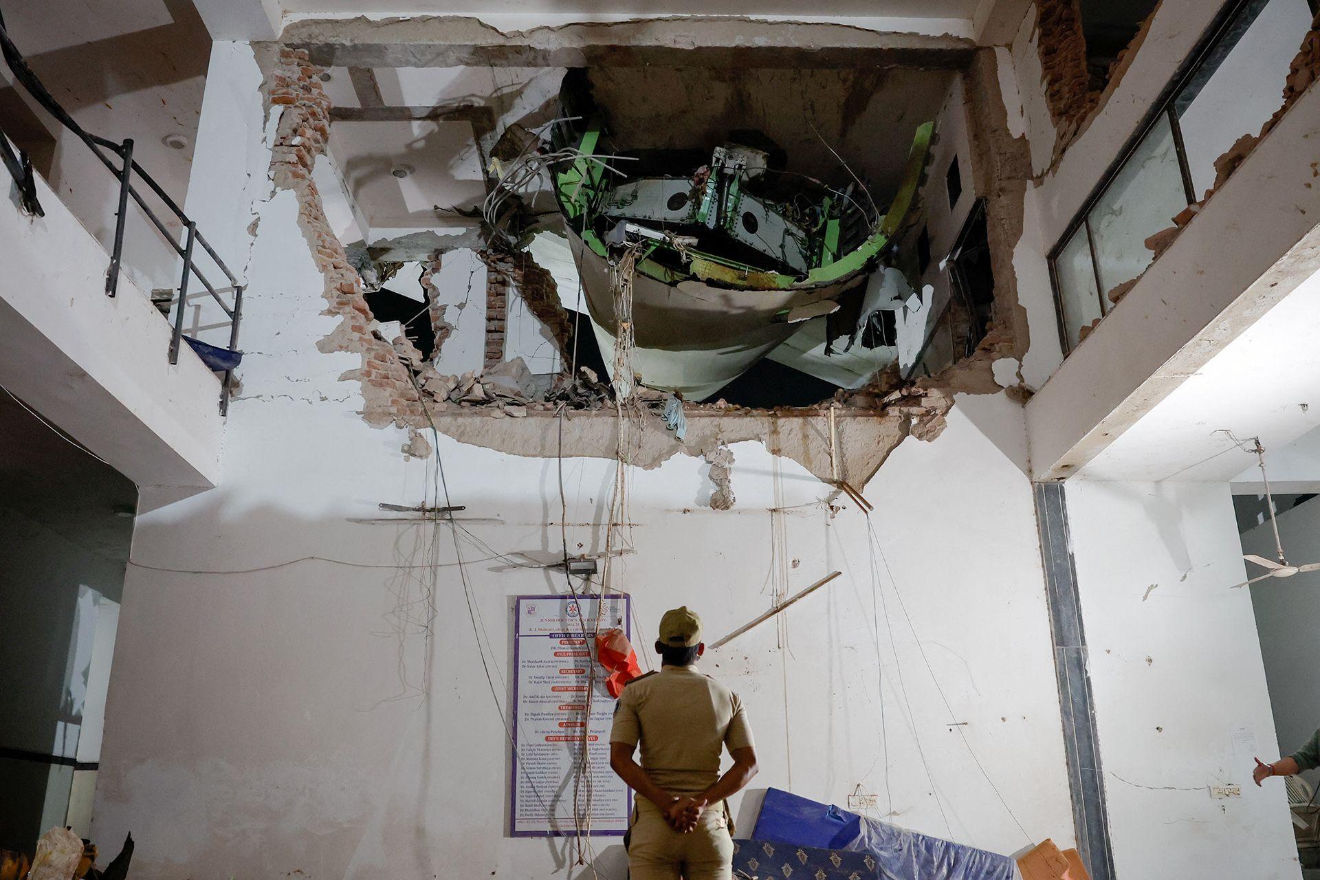 An official looks up with his arms behind his back and back turned to the camera, as they inspect a huge hole in the wall of a building interior, with some of the plane visible in the hole, on Thursday.