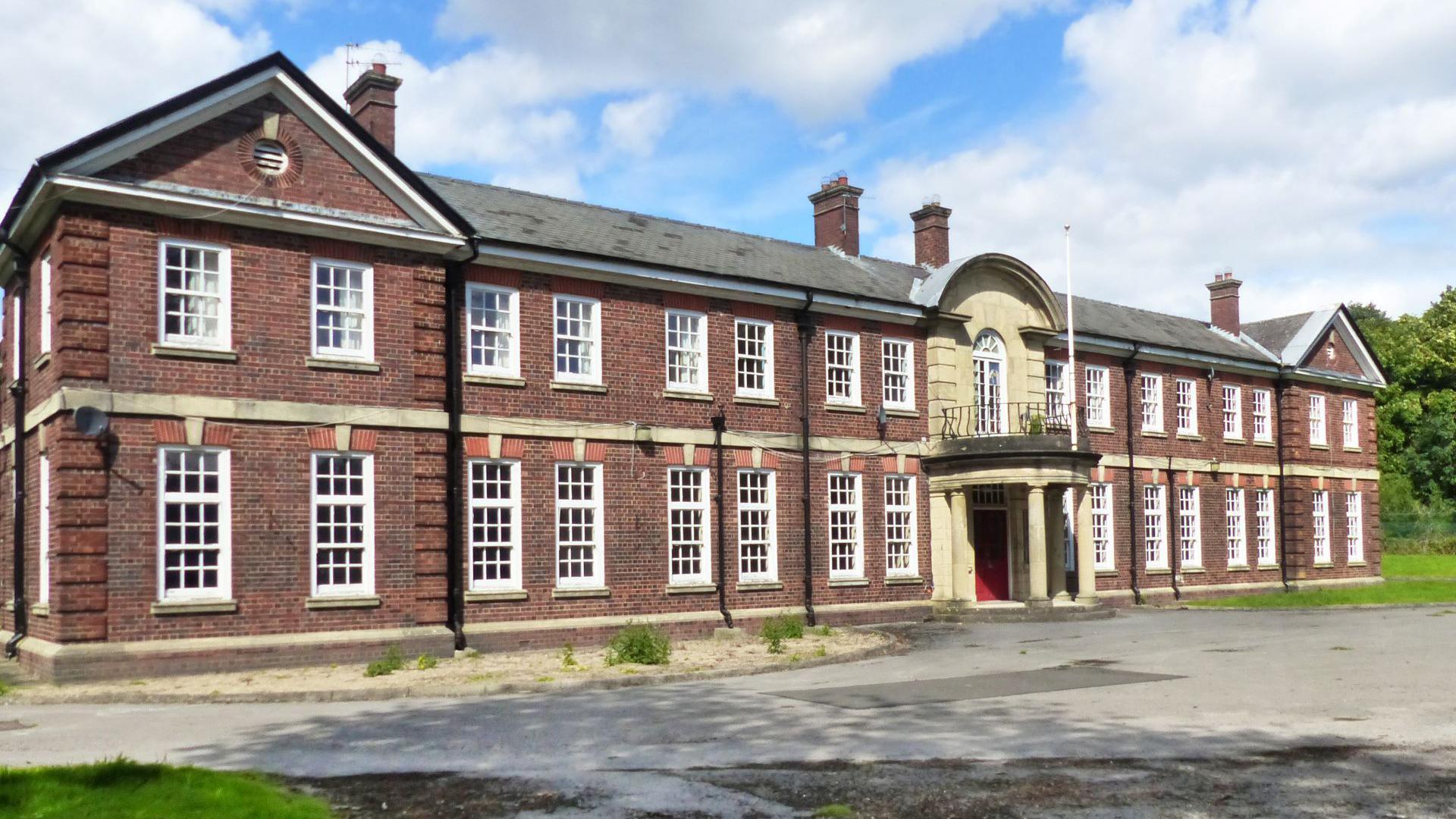 A brick building with lots of windows and a flag pole above a central porch