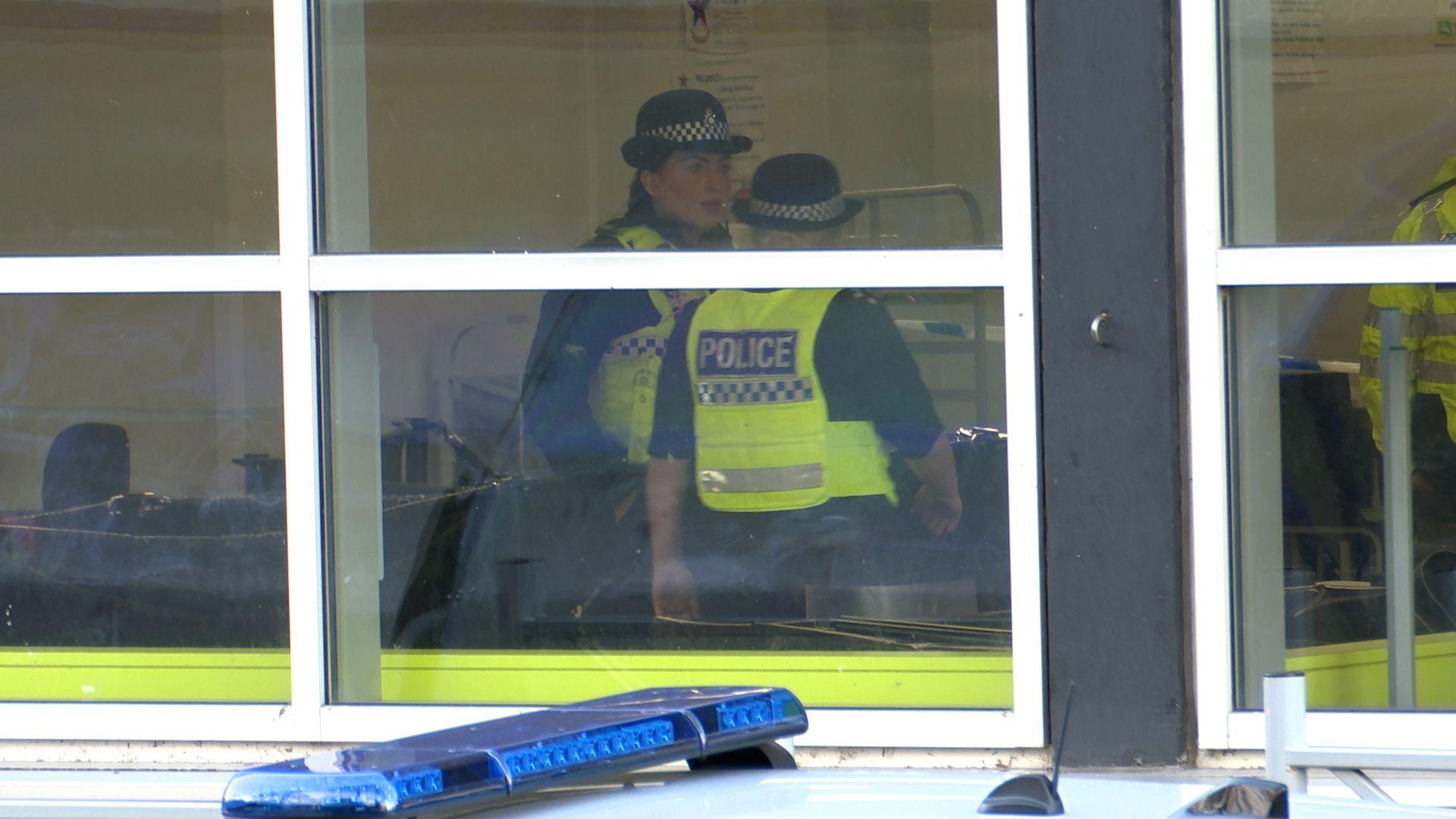 Two officers can be seen standing at the window. A police car is parked outside it but only its lights are visible.