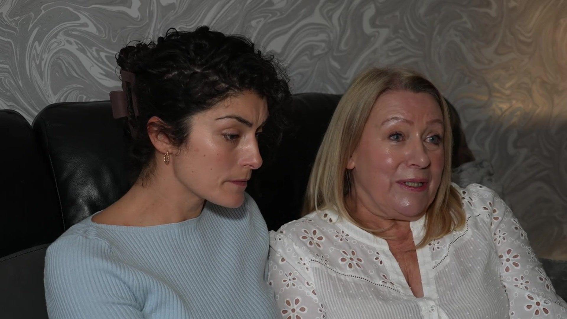 Holly Morgan, wearing a light blue jumper and her mother-in-law Jan Morgan, wearing a white top, sit on a sofa together. They both look very upset.