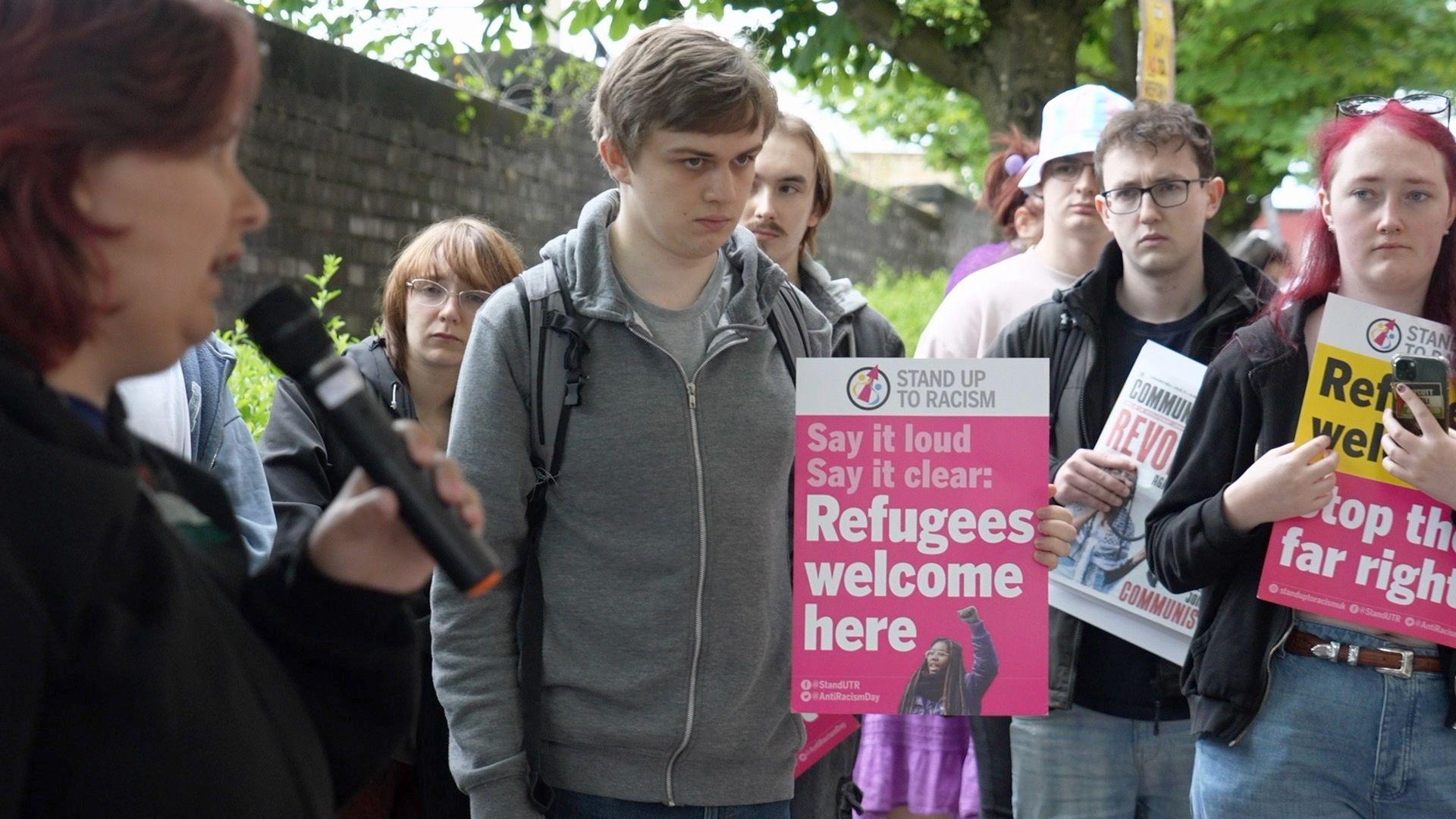 A group of protestors outside the new councils' first meeting, some holding placards. One of the placards reads: "Say it loud, say it clear: Refugees welcome here"