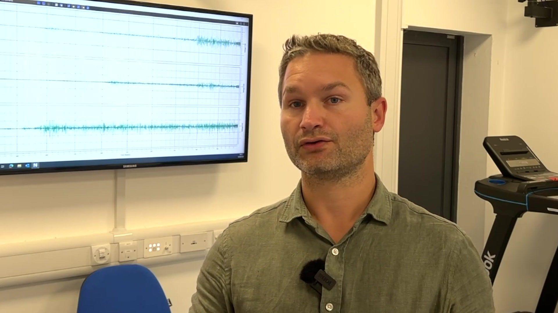 Peter Worsley, wearing a green shirt, stands in front of a screen showing data waves