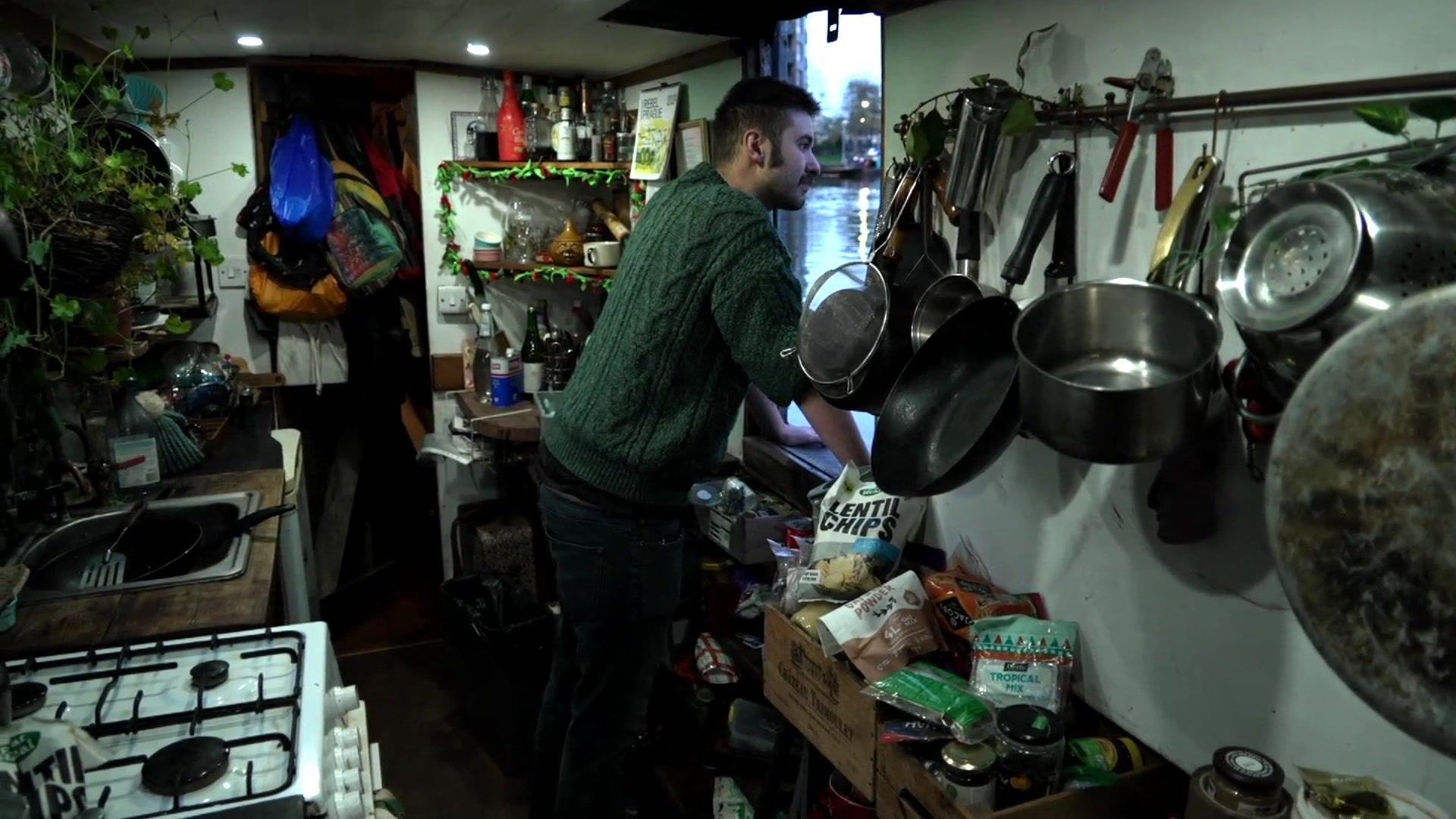 A man looks out of the window of a crowded houseboat onto the river