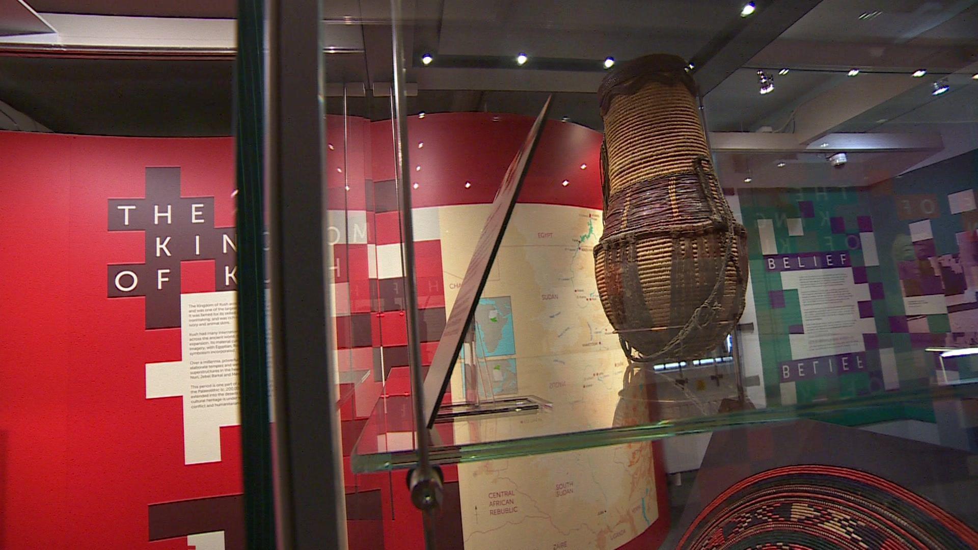 A wicker container inside a glass box, with a wall in the background with information about Sudan on.