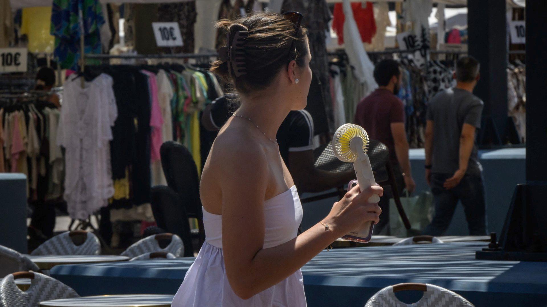 A woman cools herself with a handheld electric fan