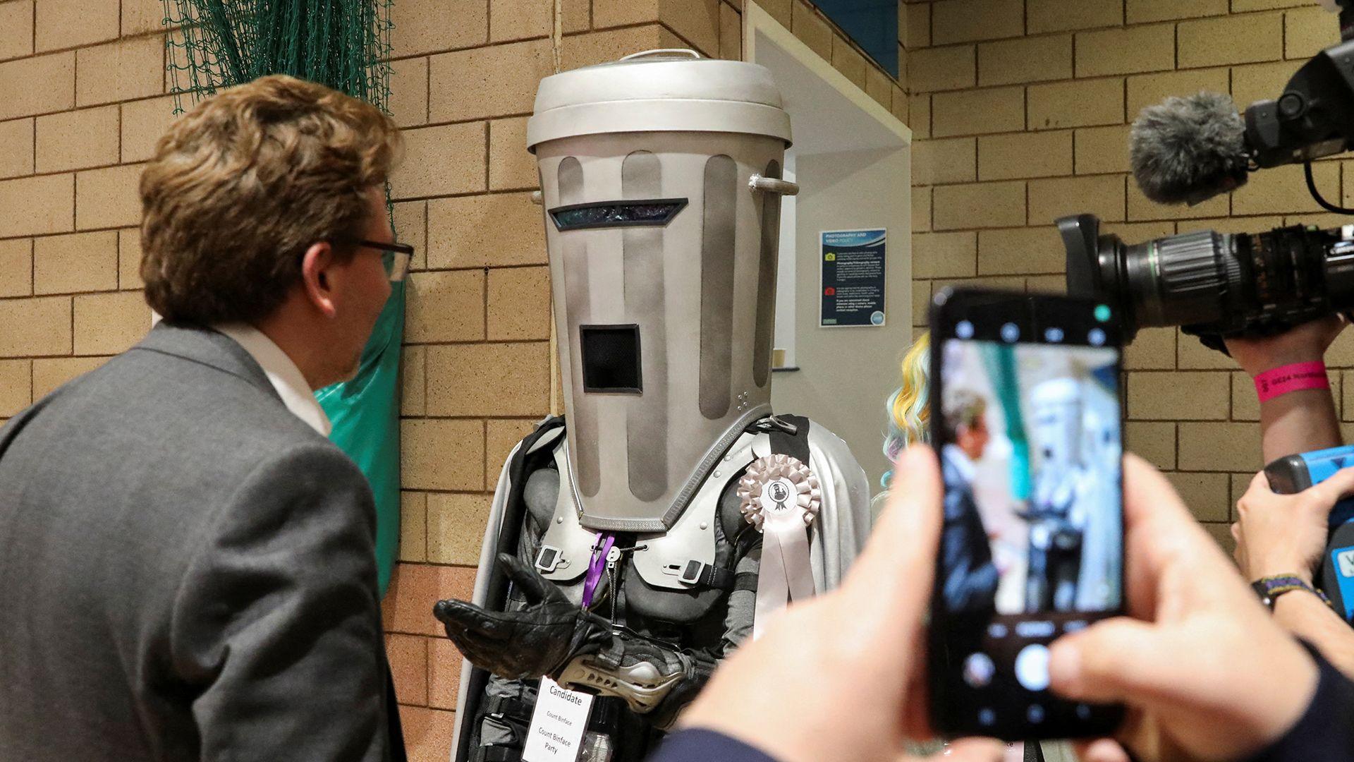 A person wearing a sci-fi costume of a bin speaking to a journalist in a sports hall