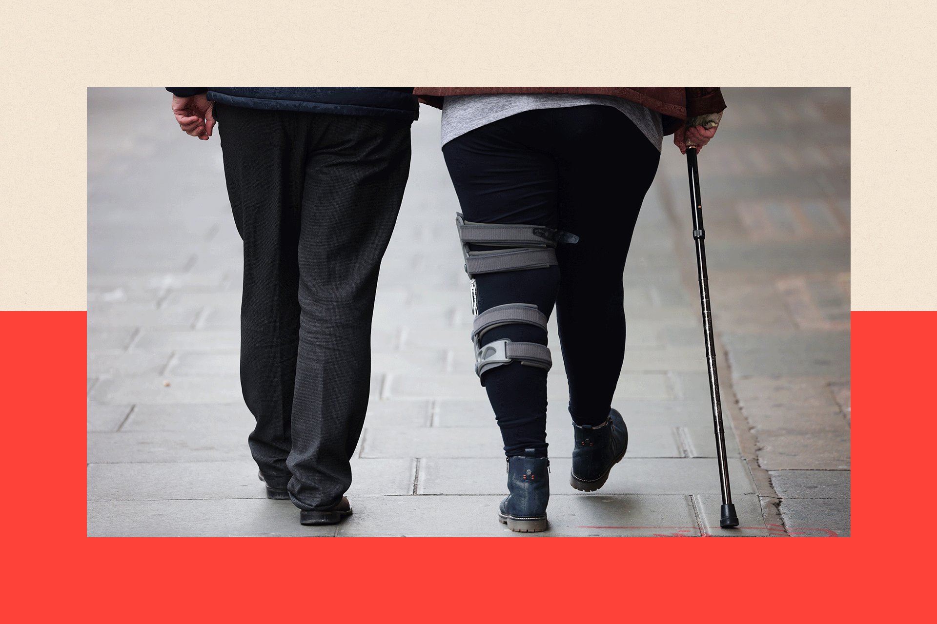 A woman with a leg brace and a walking stick walks alongside a man, only the bottom half of their legs showing