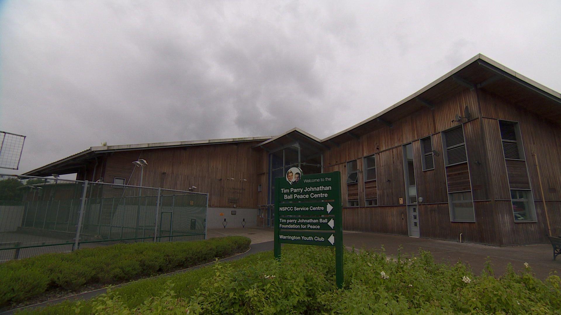 External shot of the peace centre, a wooden building with grassy areas in front and a fenced off area