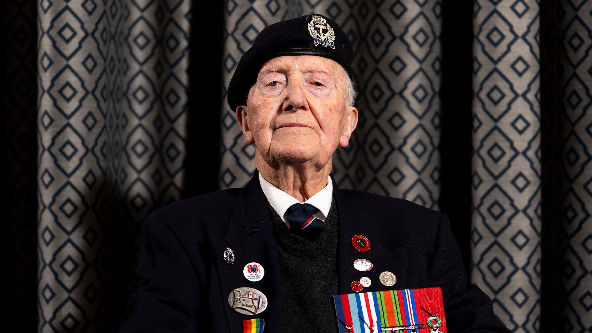 Royal Navy veteran Stan Ford - wearing a suit and naval beret - looks down the camera lens.