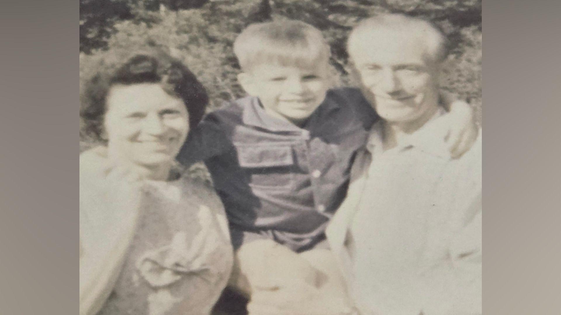 A black and white image of a man and a woman with a young boy in the middle of them. They are all smiling at the camera. 