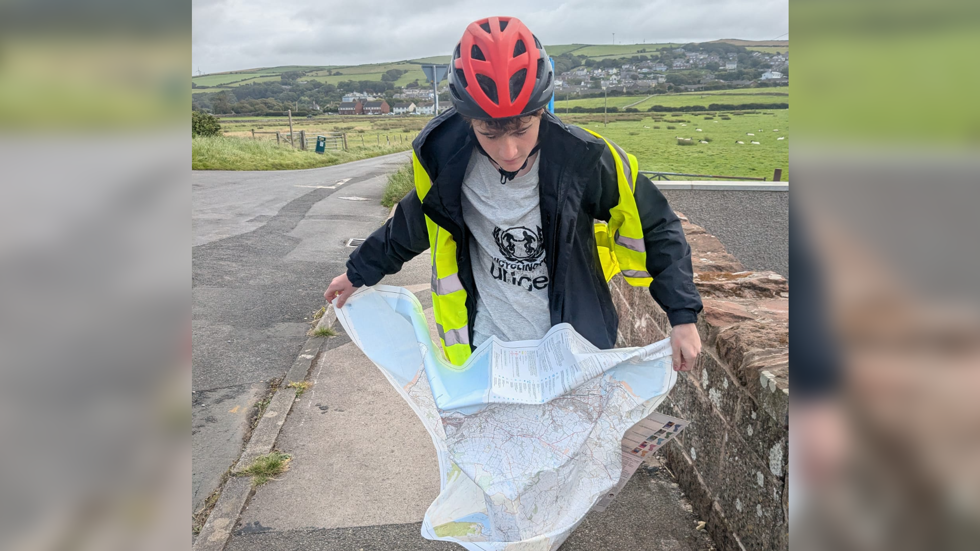 Jim wears a cycling helmet and T-shirt with the Unicef logo on, as well as a high-visibility jacket. He is reading an Ordnance Survey map.