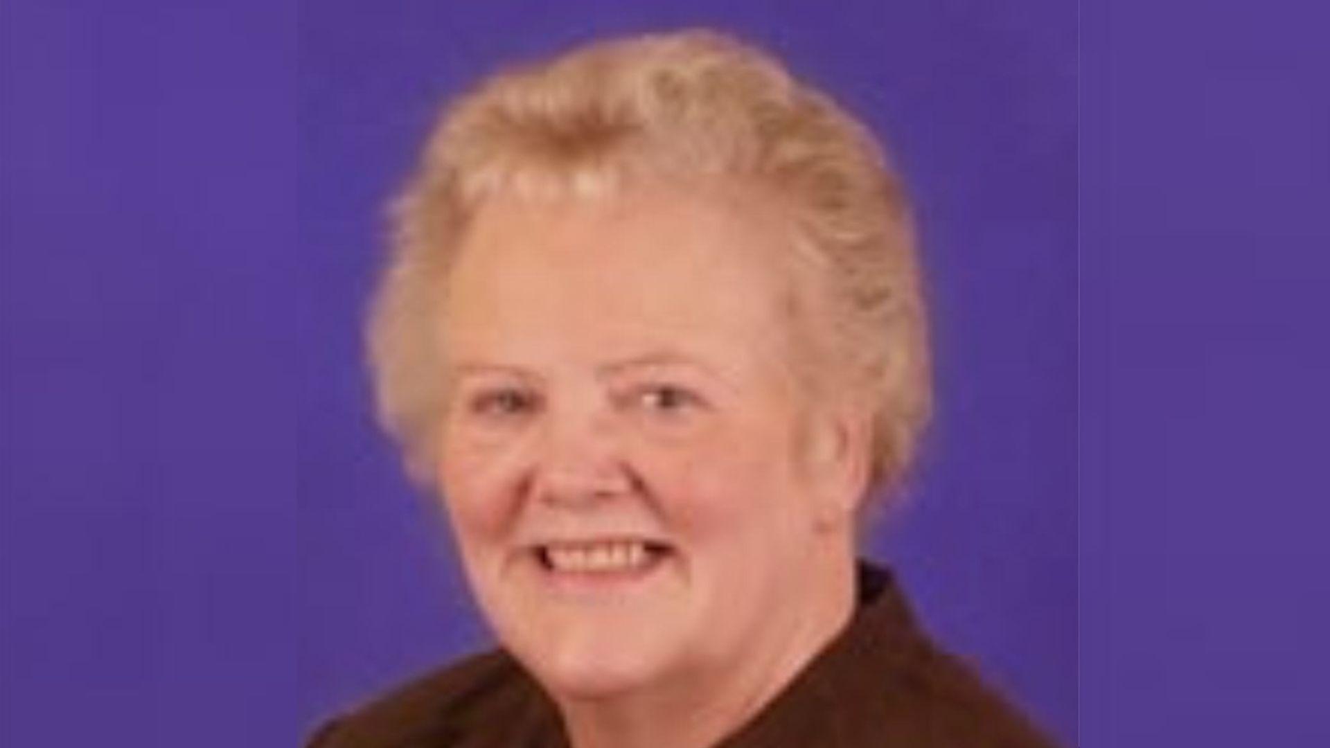 Councillor Paddy Bradley smiles towards the camera. She has light-coloured hair and is wearing a dark blouse. There is a purple background