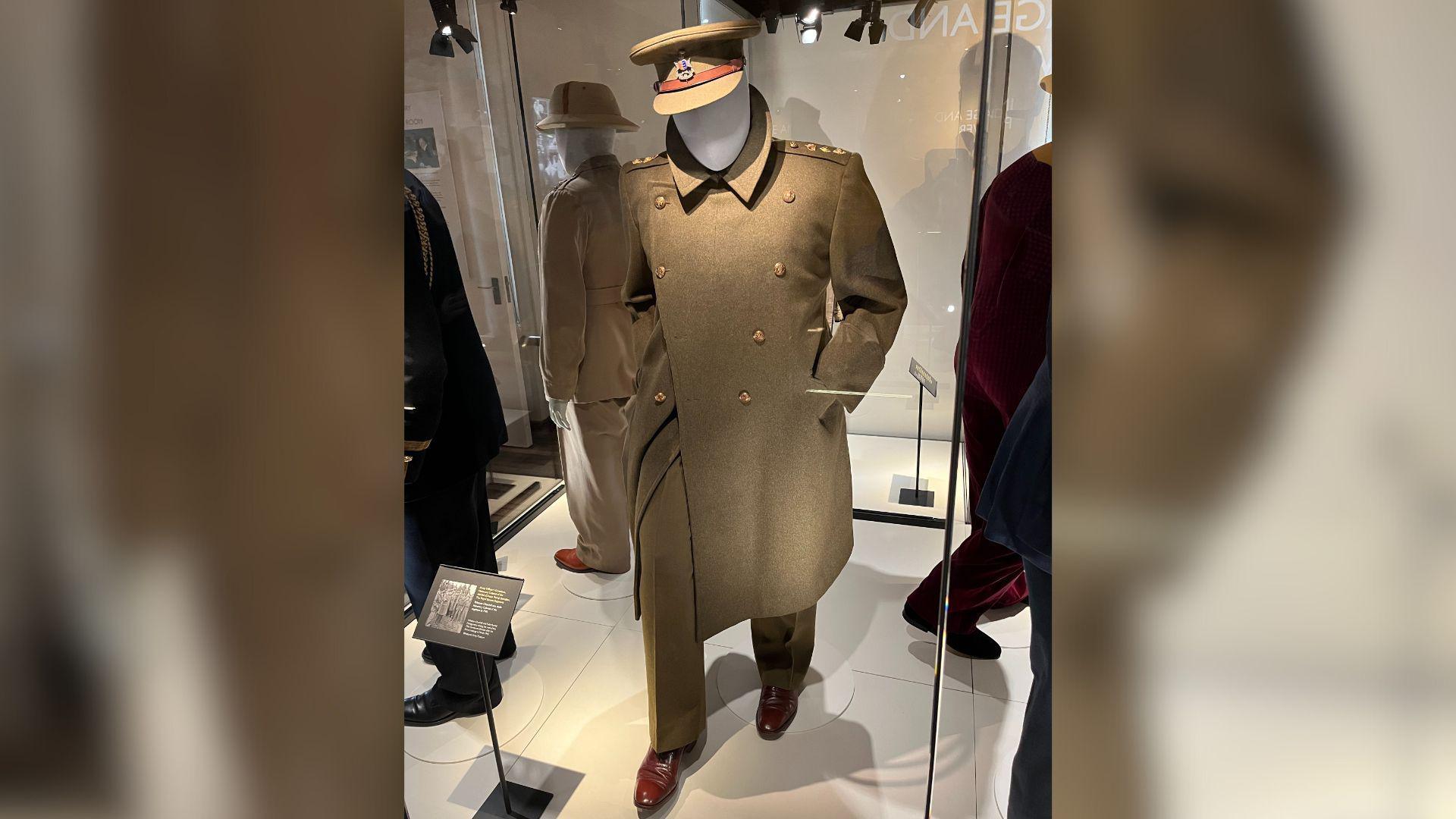 A large green army officer's coat from the Second World War on a mannequin, also dressed in green trousers and a green army officer's hat. The mannequin is in a glass display box