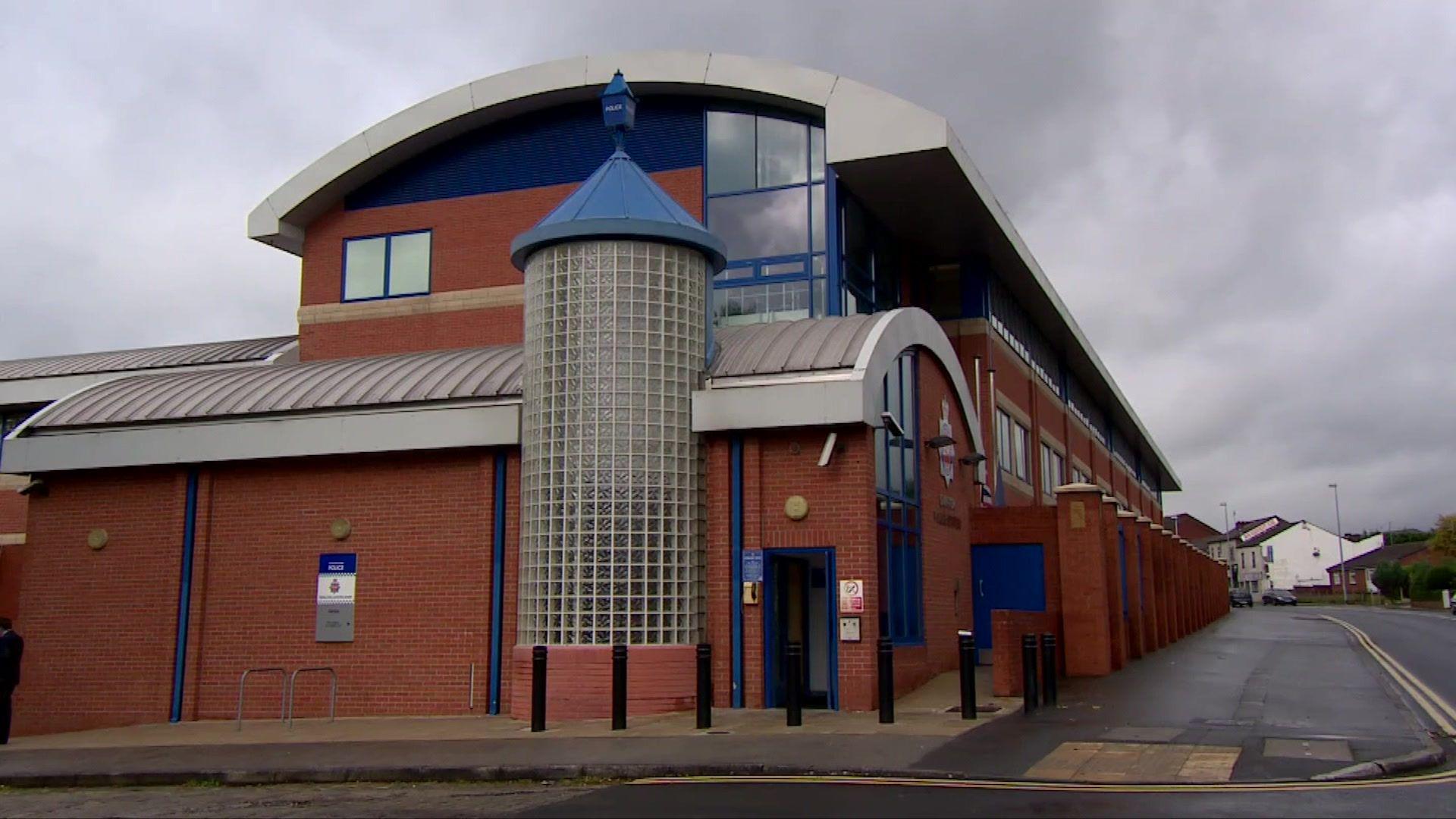 A red brick building on the corner of the road with blue doors and window frames, with police emblem on