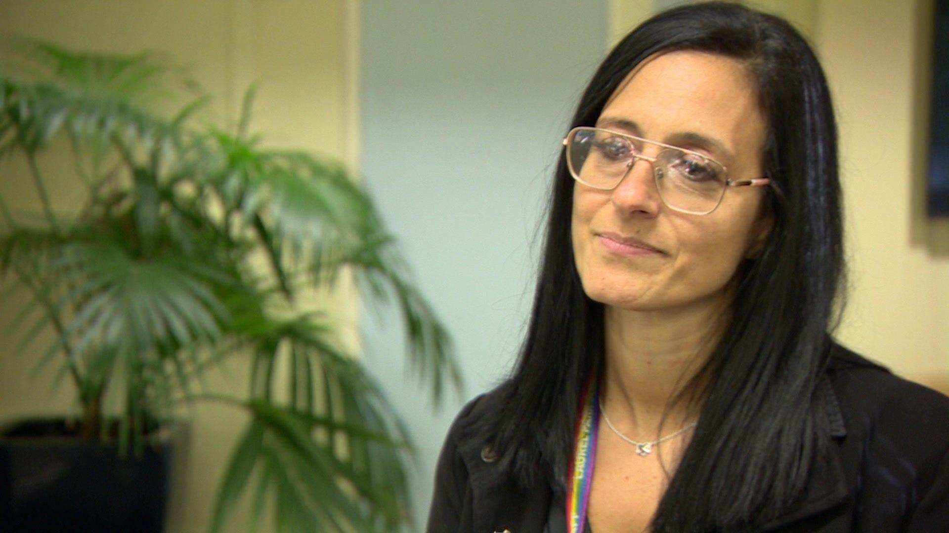 Dark-haired woman wearing glasses with a plant in the background