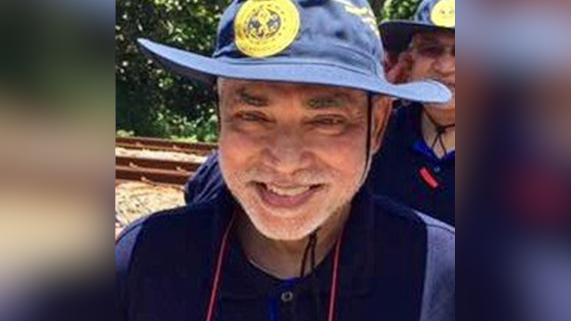 Dr Kumararatne is smiling at the camera while standing outside on a sunny day. He is wearing a navy hat and matching shirt.