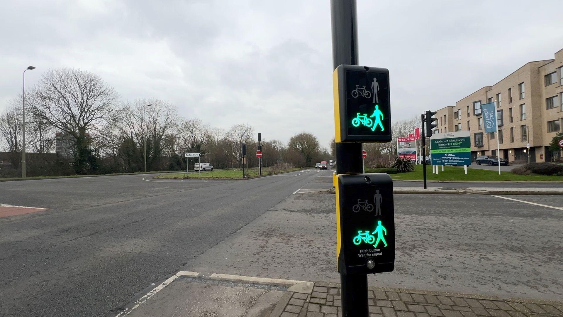 The crossing, with the display showing green, with symbols for pedestrians and cyclists to cross. The view of the Ring Road looks in the direction of Summertown, with new Barton Park flats visible on the right.