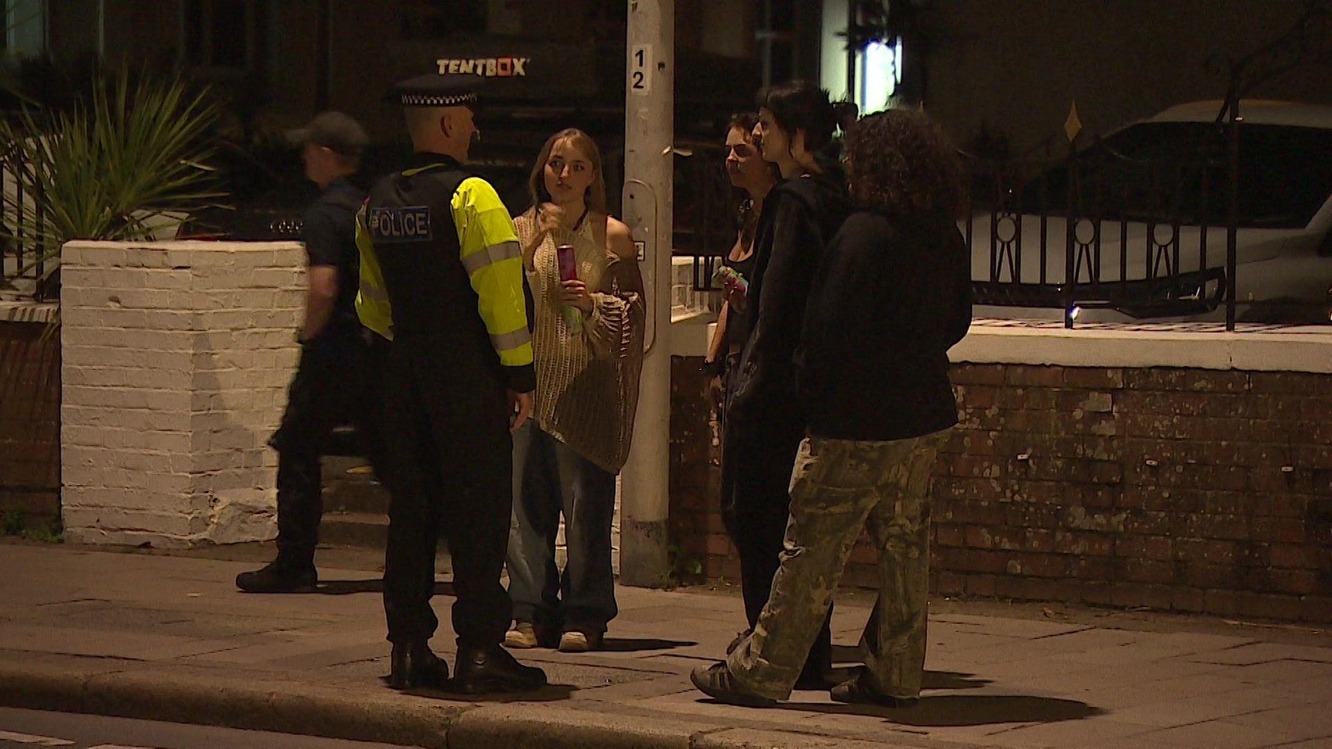 A police officer speaking with three young people standing on a pavement after dark