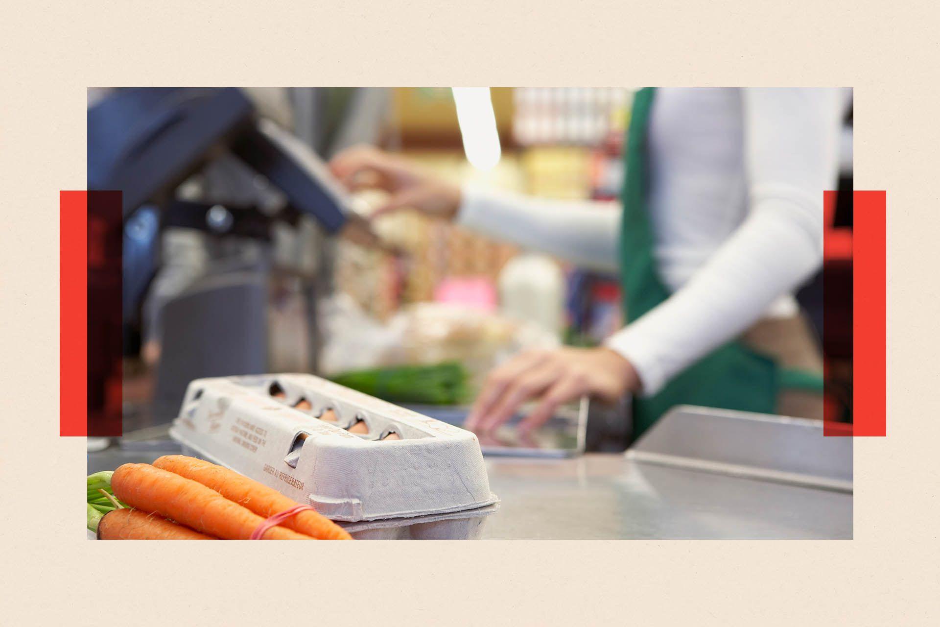 A casher at a supermarket processes a carton of eggs and a bunch of carrots