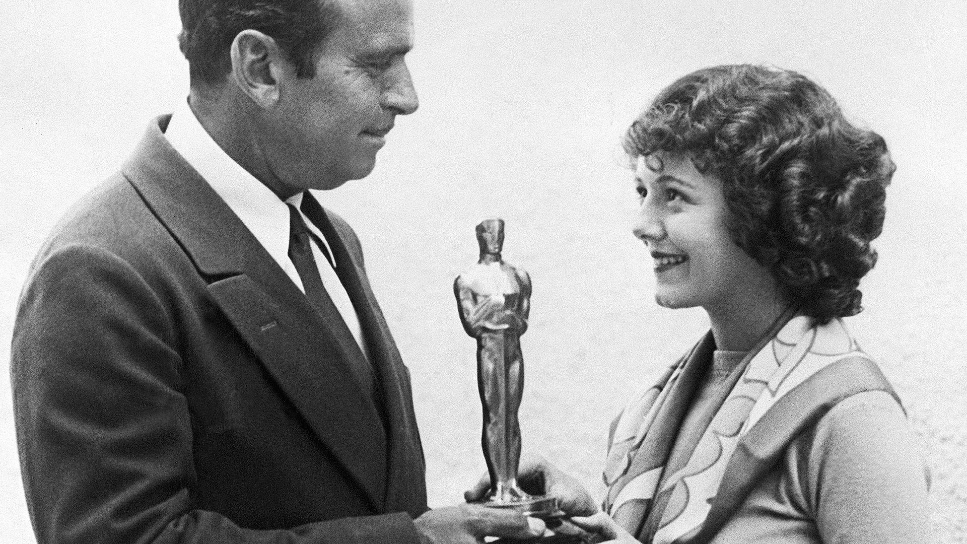 A man in a suit presents an actor with a gold statue of a person